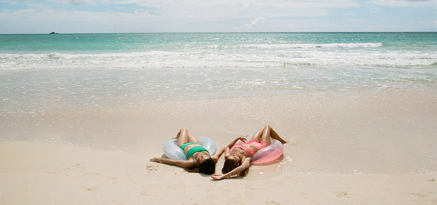 Two people lying on inflatable rings on a sandy beach with ocean waves in the background