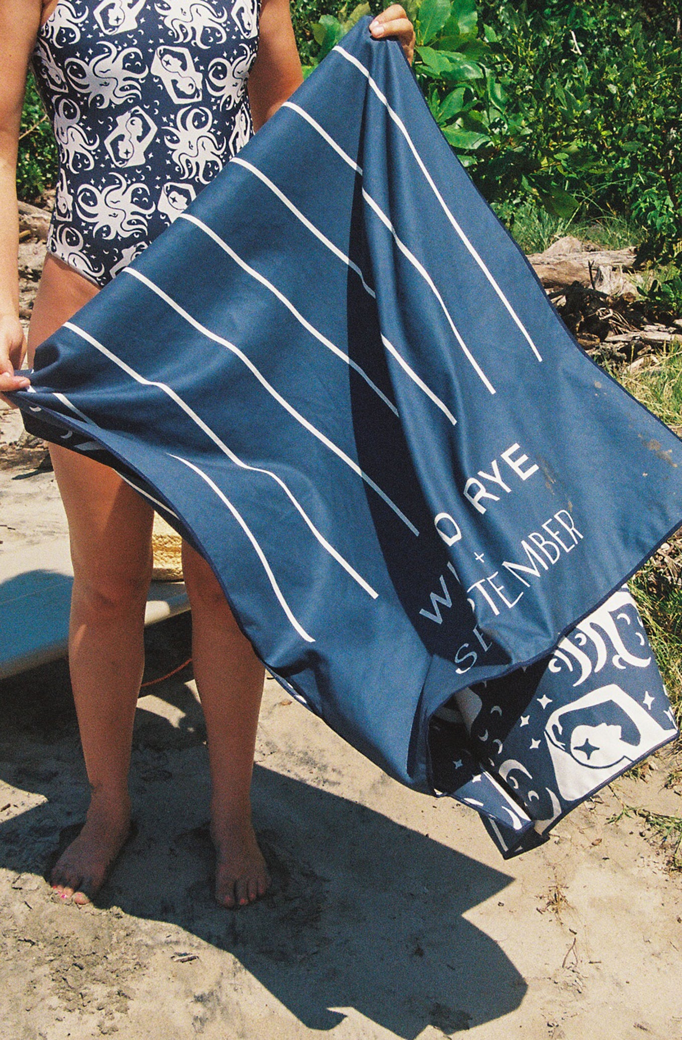 Person holding a blue towel with white stripes and branding outdoors.