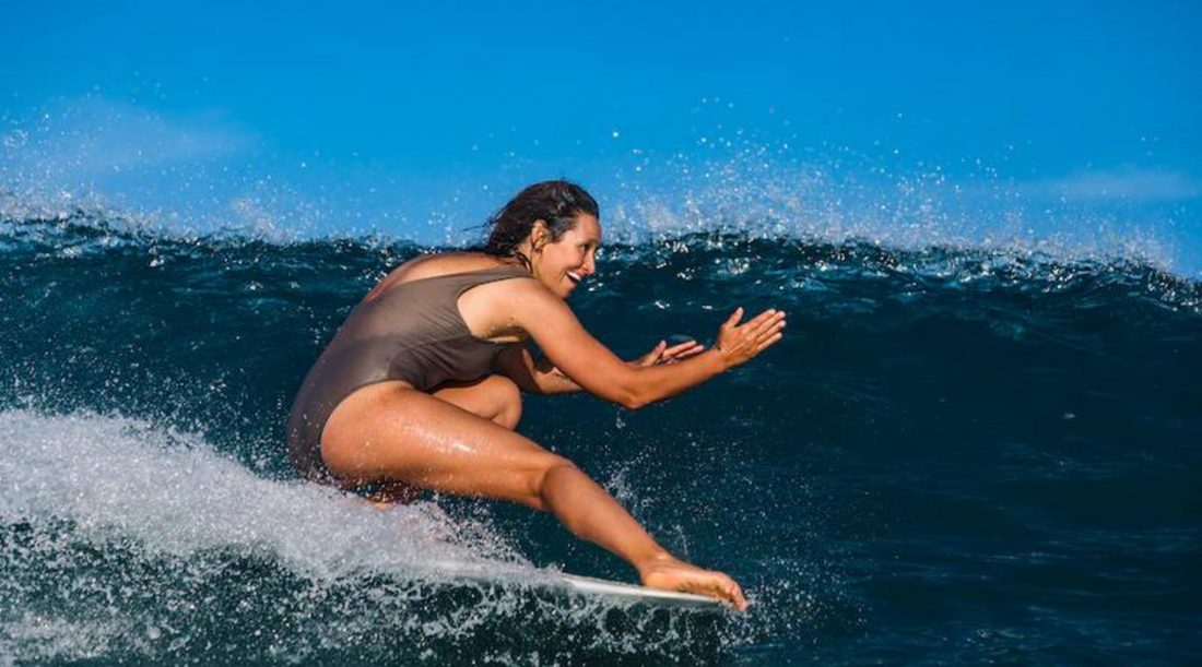 Kassia Meador doing a cheater five wearing a one piece surf swimsuit