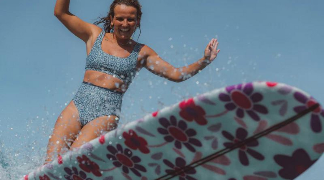 Woman doing a bottom turn on pink longboard wearing Grace surf bikini top and elise bikini bottom in army