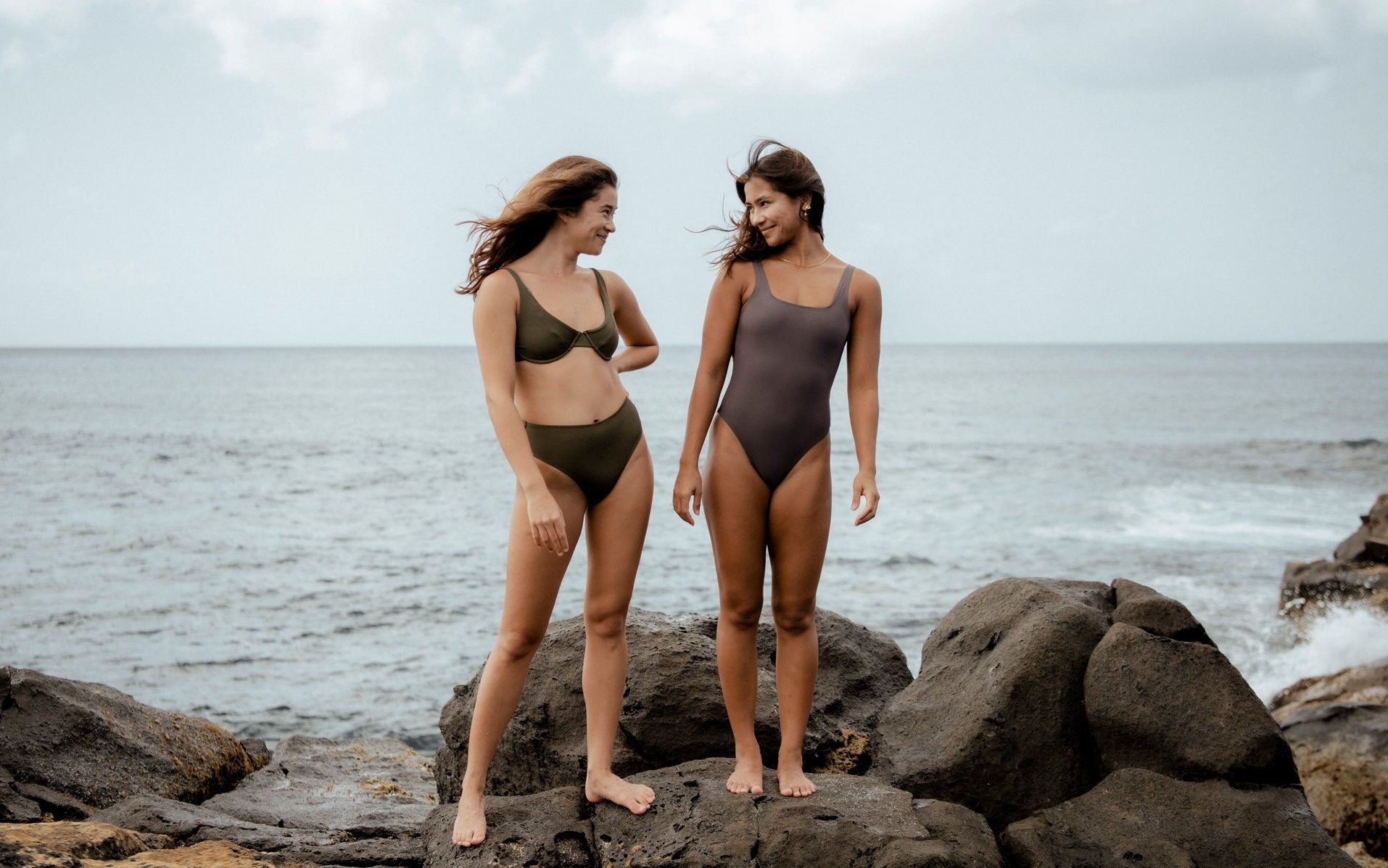 Two women wearing swimsuits standing on rocks