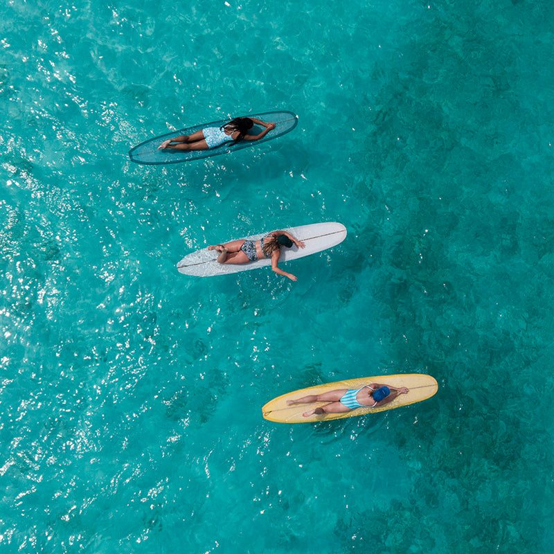 Three people on surfboards in clear blue water from an aerial perspective