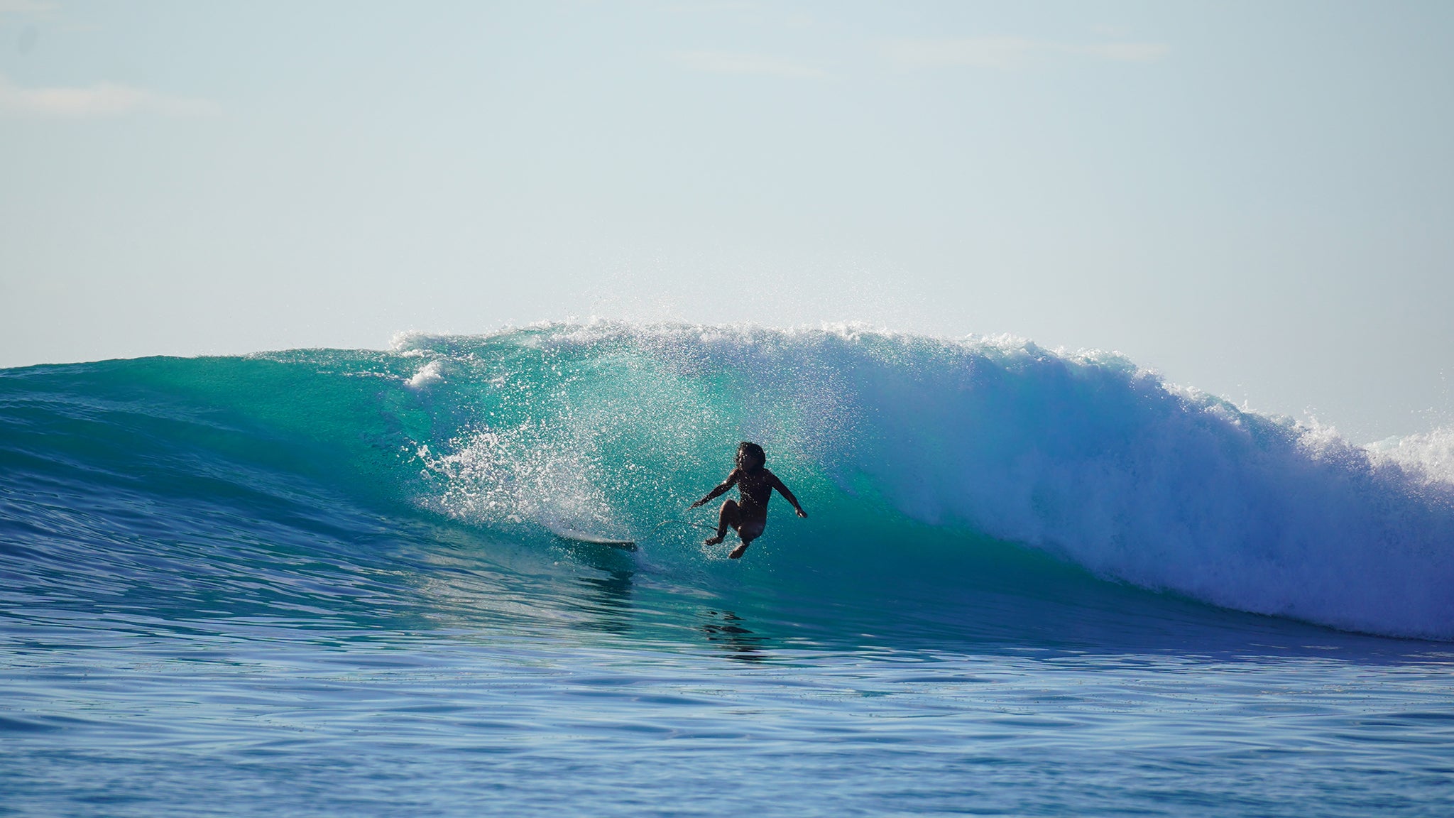 Person surfing a large wave in the ocean with clear blue sky.