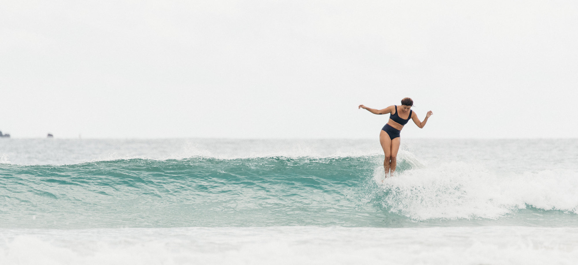 Lola Mignot nose riding facing the beach wearing the Eden surf bikini to and Lucky surf bikini bottom in Black