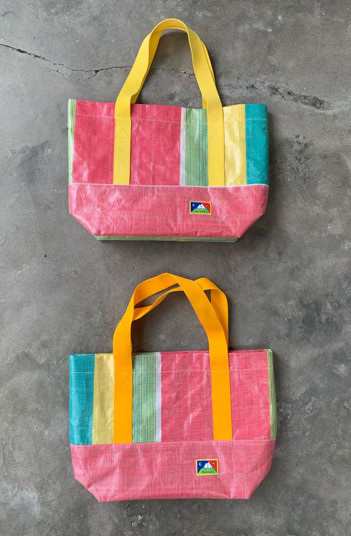 Two Bingin tote bags colorful striped tote bags on a gray concrete surface.  Bingin tote bags