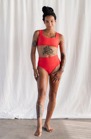 Person wearing a red swimsuit standing against a white curtain