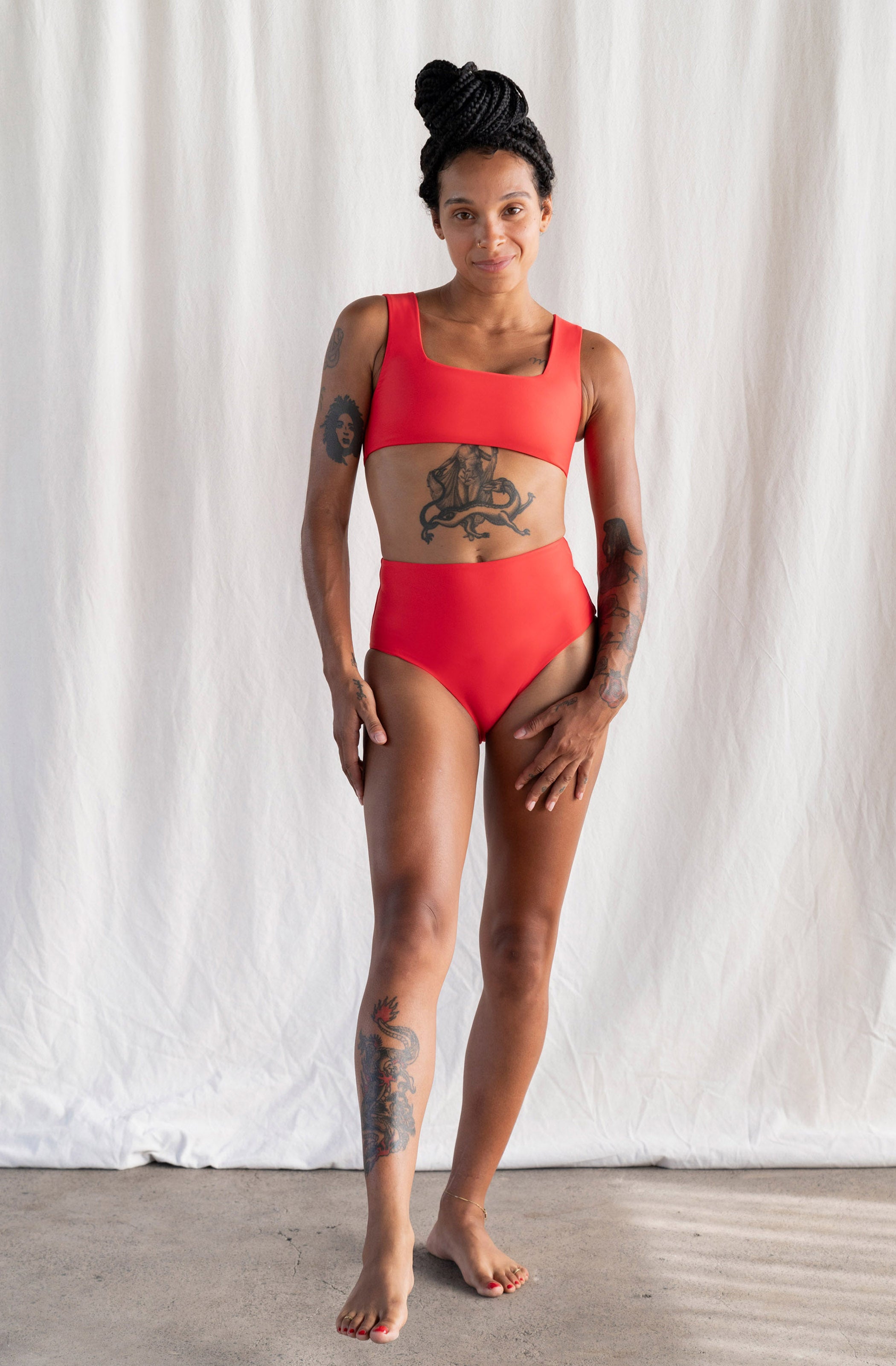 Person wearing a red swimsuit standing against a white curtain