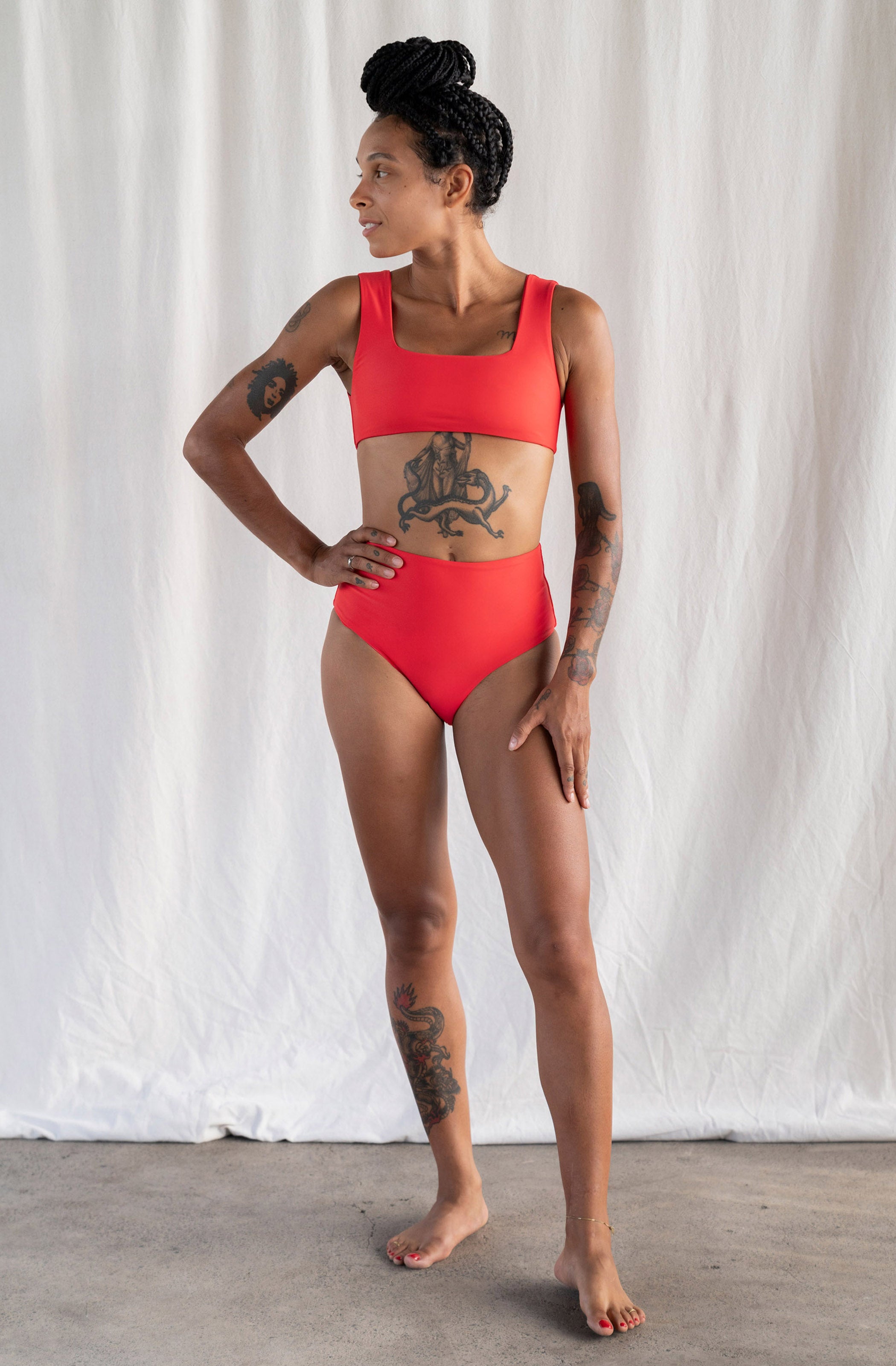Woman wearing a red swimsuit standing against a white curtain.