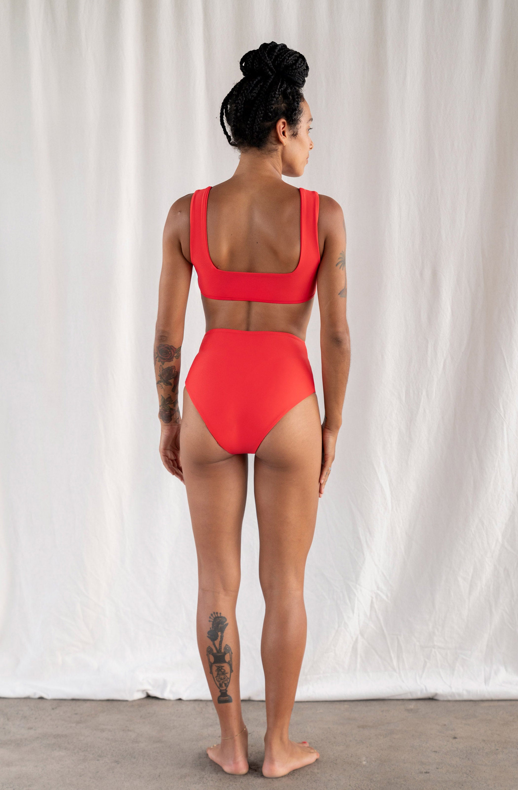 Person wearing a red swimsuit standing against a white curtain.
