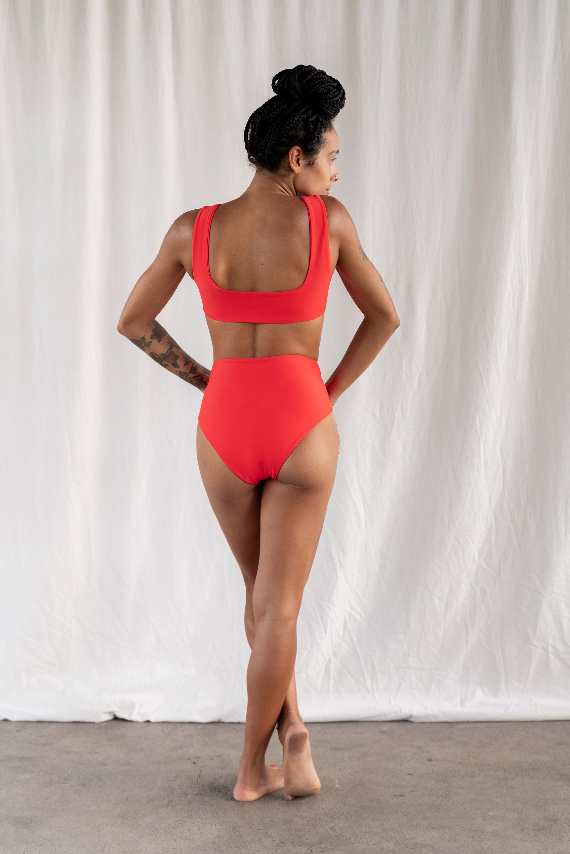 Woman wearing a red swimsuit standing against a white curtain.