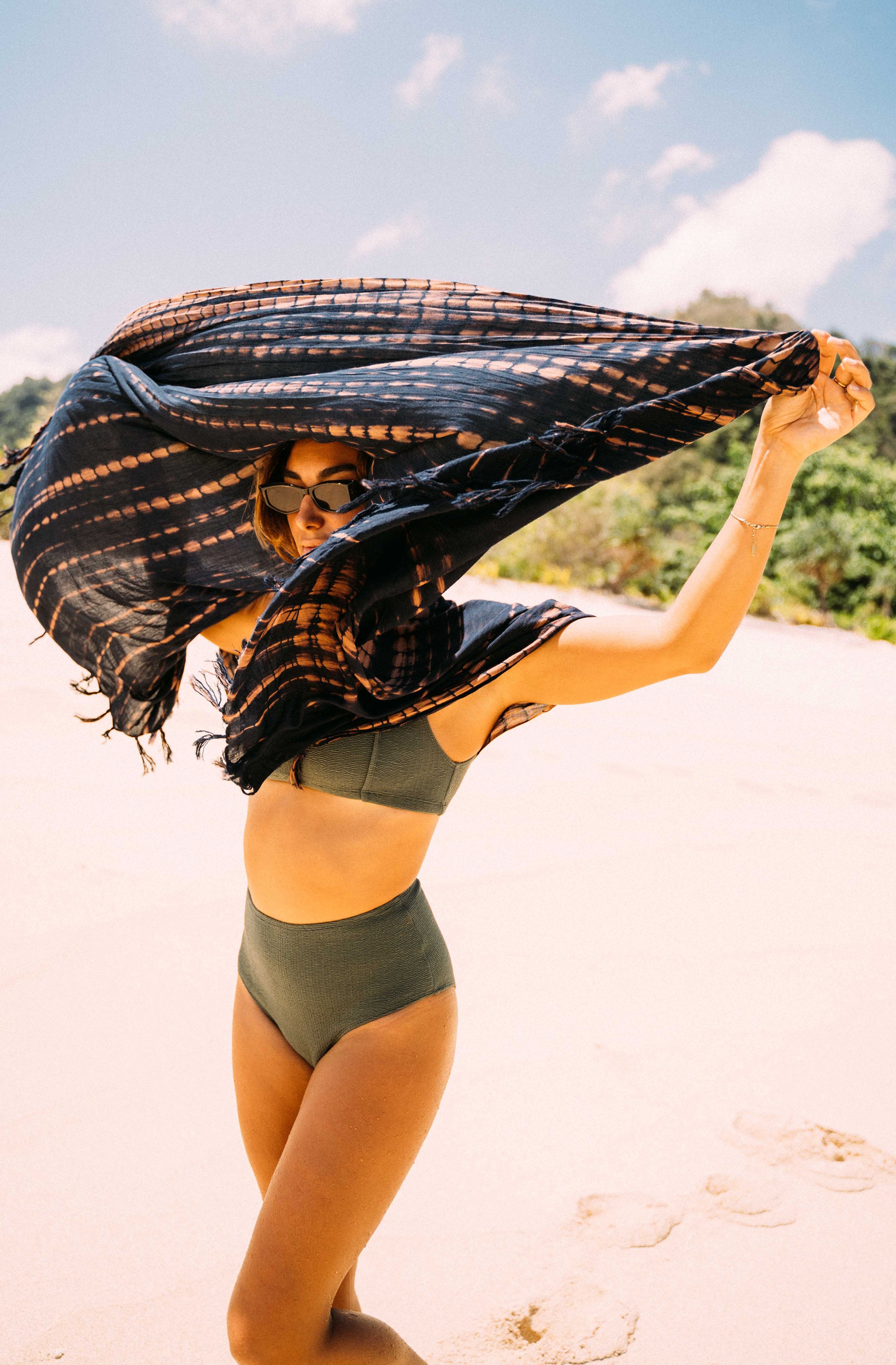 Woman in a green bikini holding a black shawl on a beach