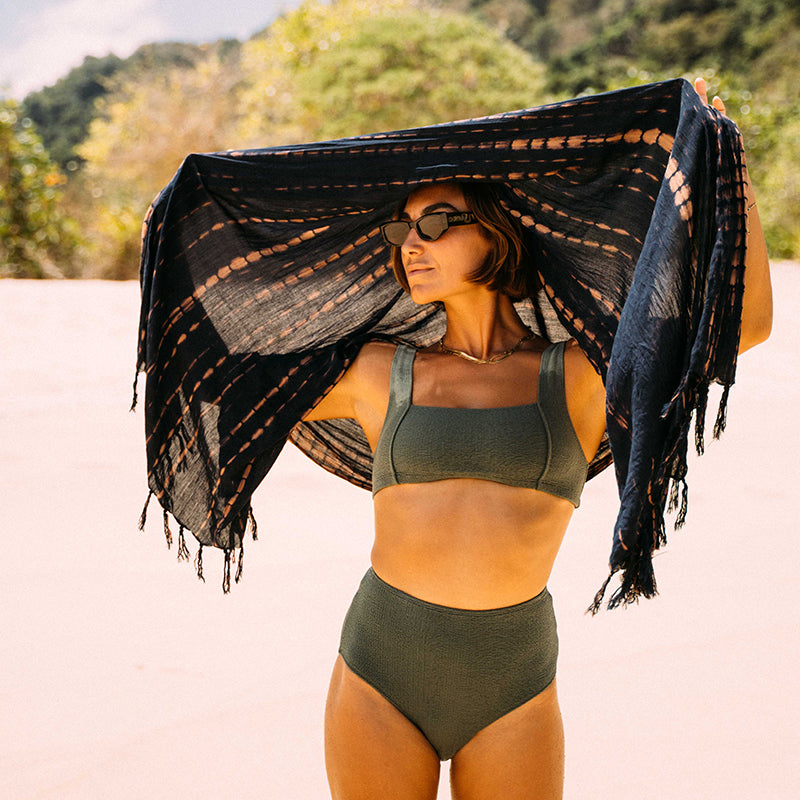 Woman in a green bikini holding a black and white patterned scarf outdoors.