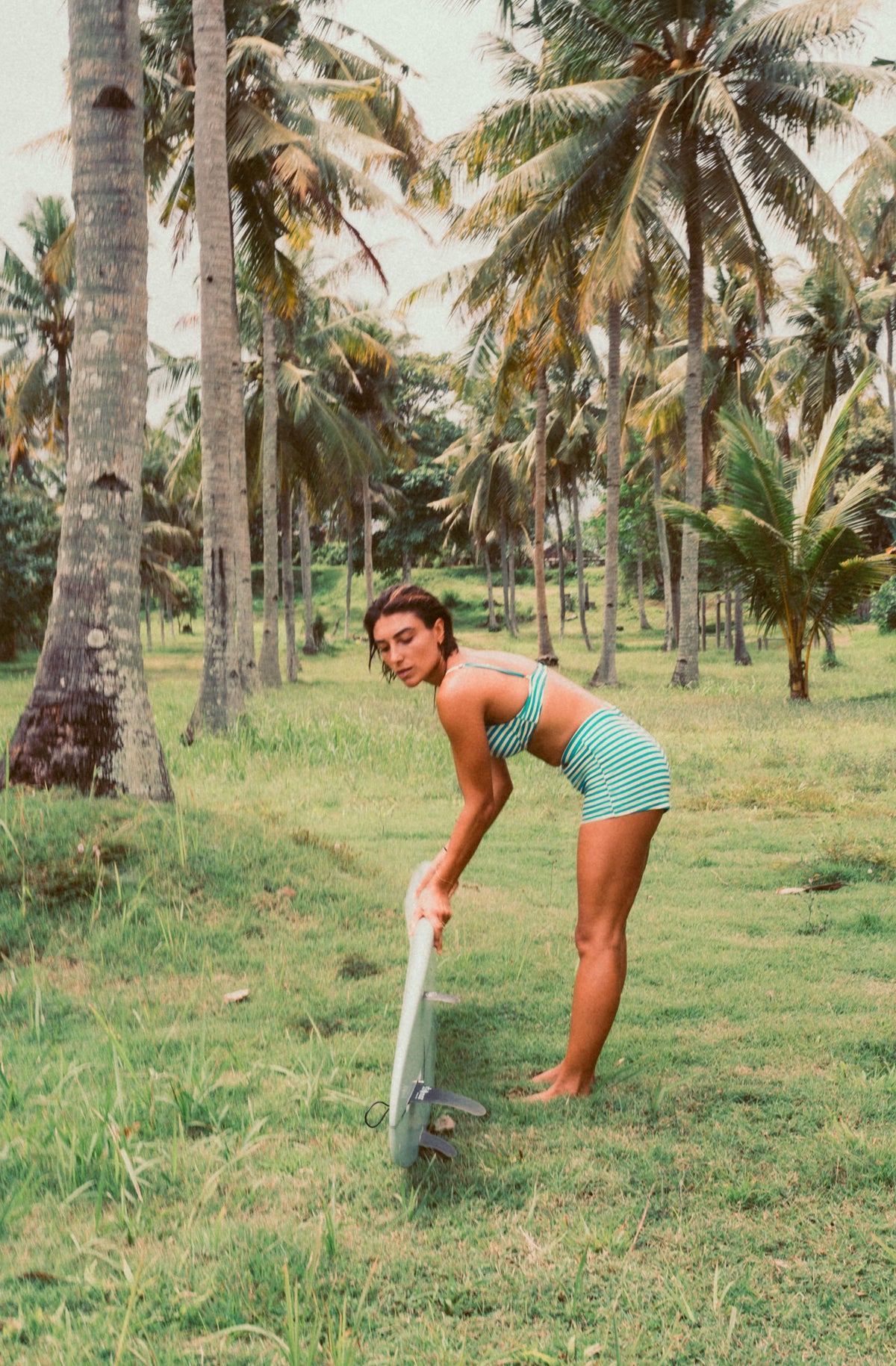 Woman in a green bikini standing in a grassy area with palm trees