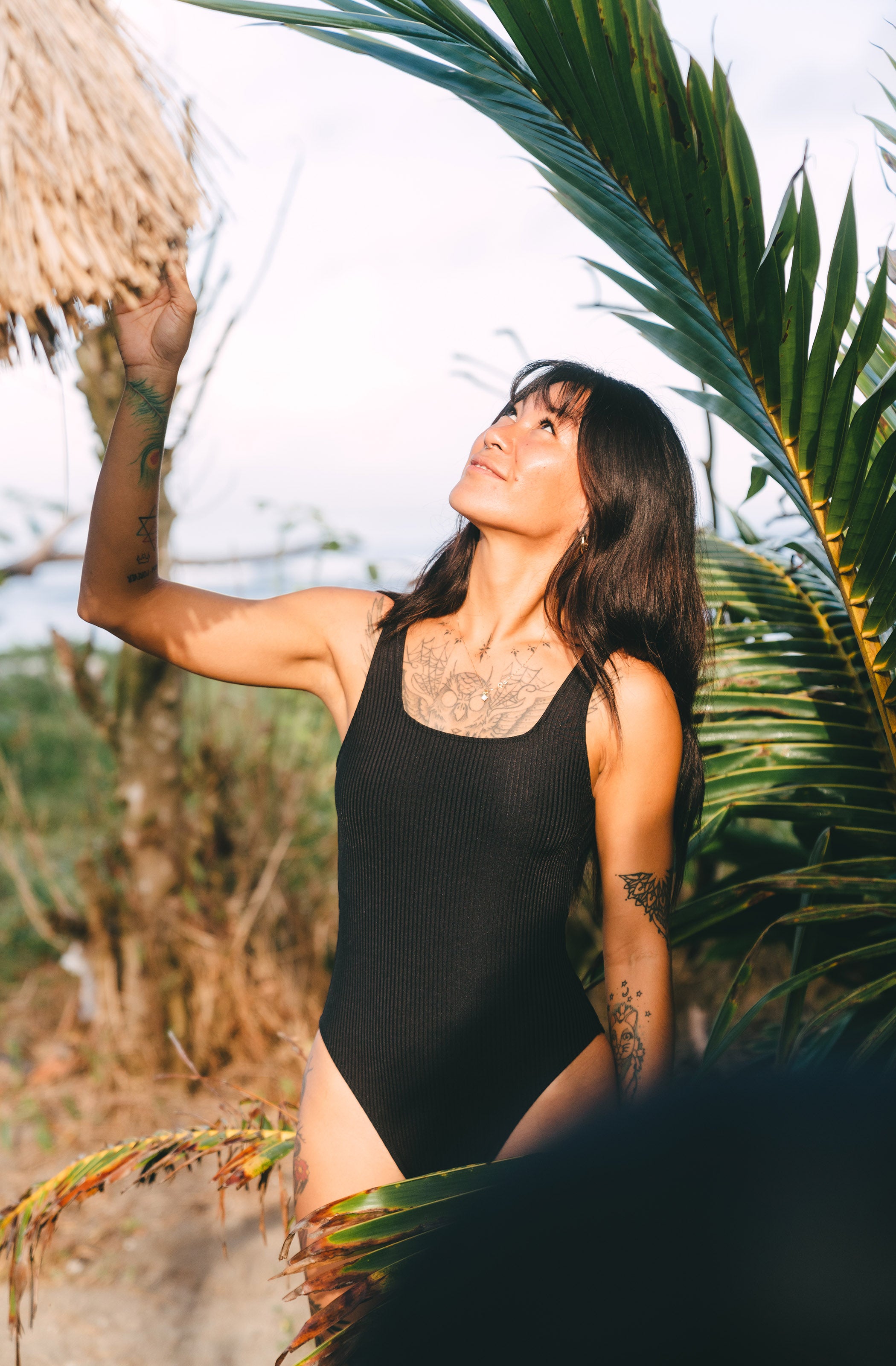 Woman in a black swimsuit standing among palm leaves