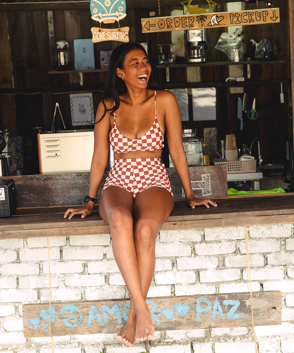Woman in a checkered swimsuit sitting on a counter with a store interior in the background.