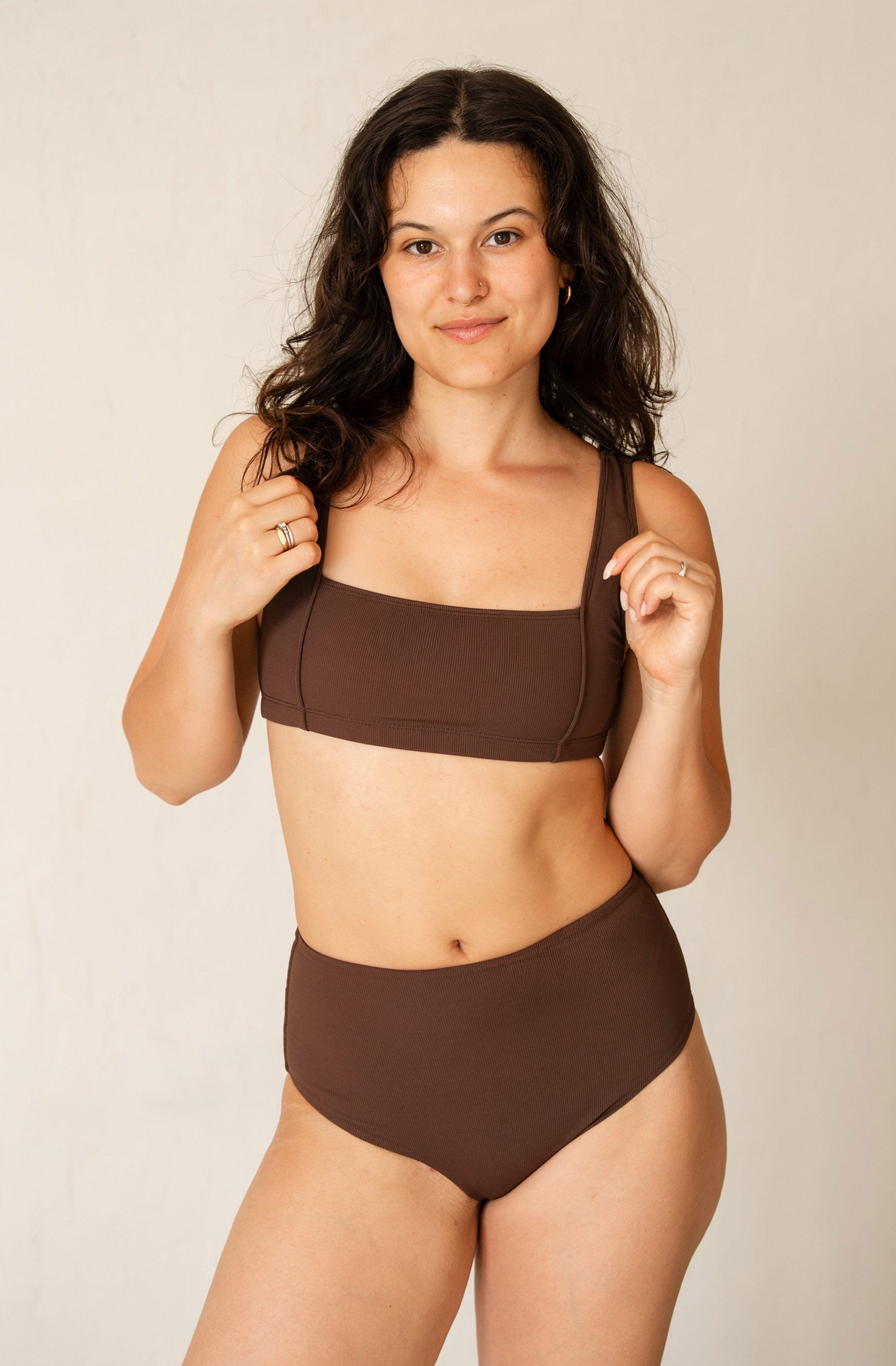 A woman modeling a solid dark brown two-piece bikini set against a plain, light beige studio background.