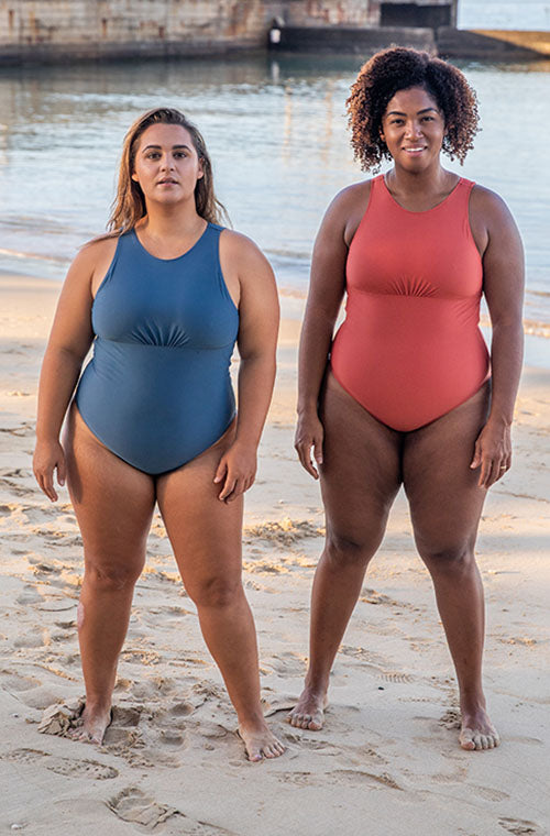 Two woman standing next to each other on the beach wearing the Ami One Piece surf swimsuit in Blue and Burnt Sienna