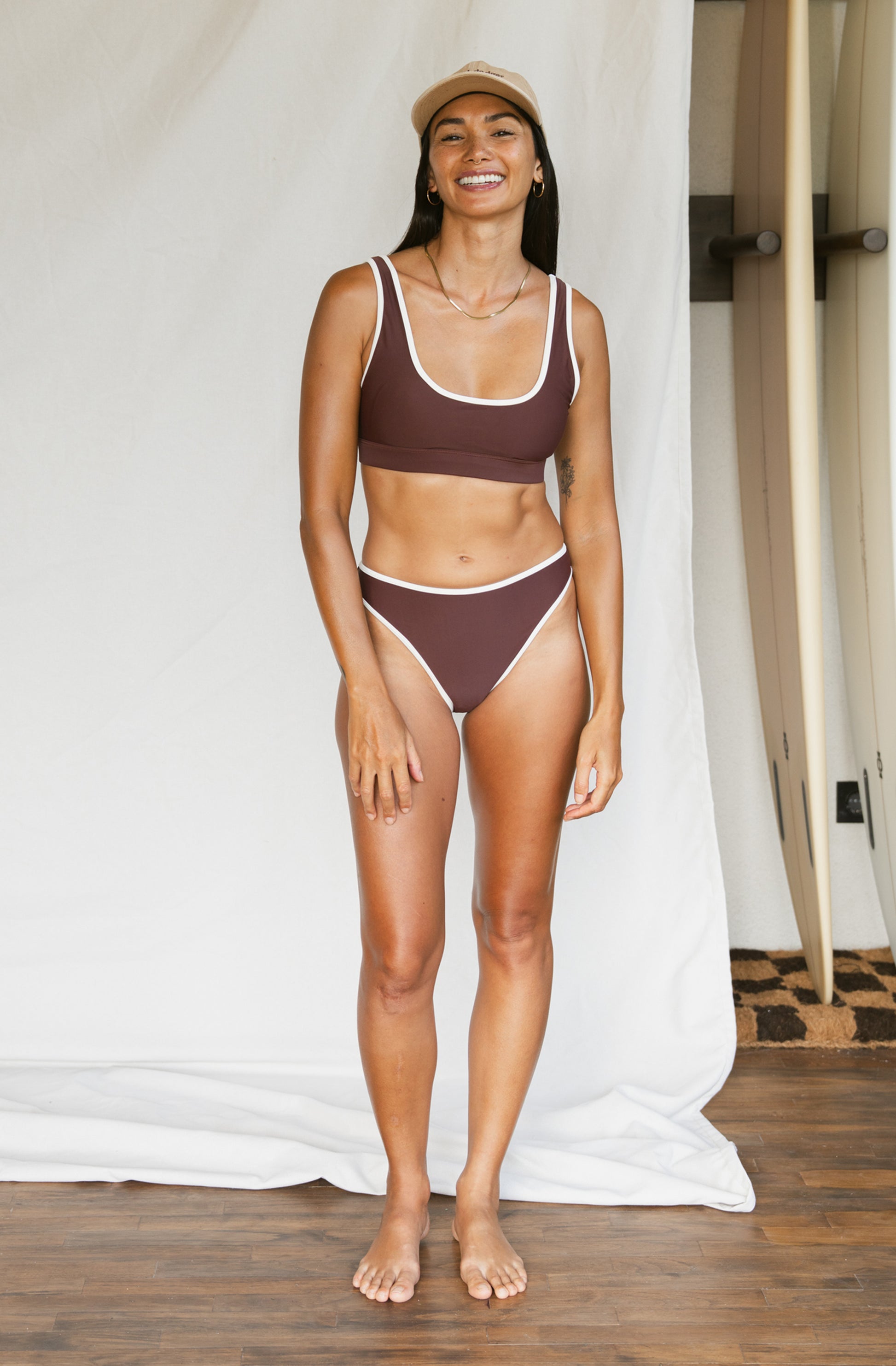 Woman wearing a brown bikini set standing against a white curtain.