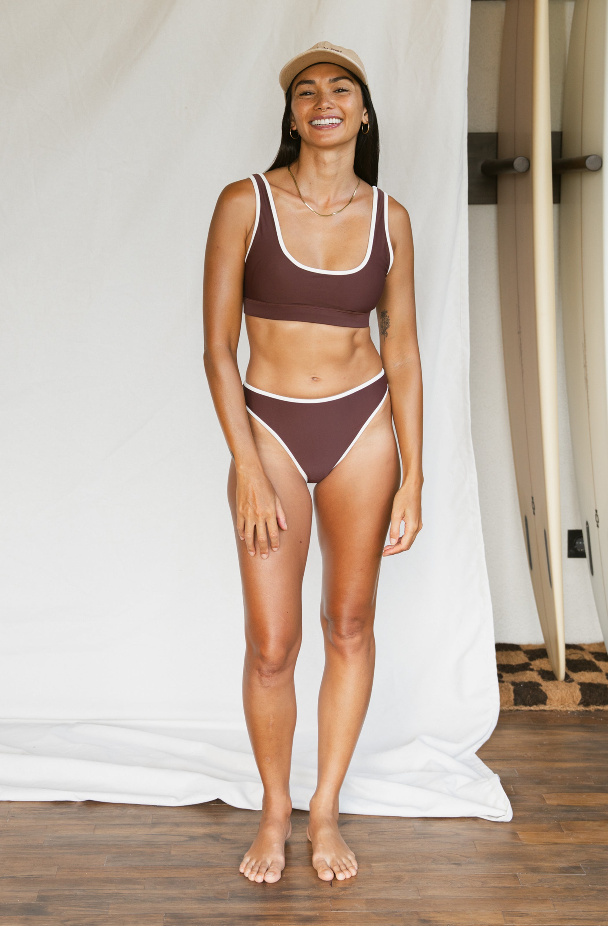 Woman wearing a brown bikini set standing against a white curtain.