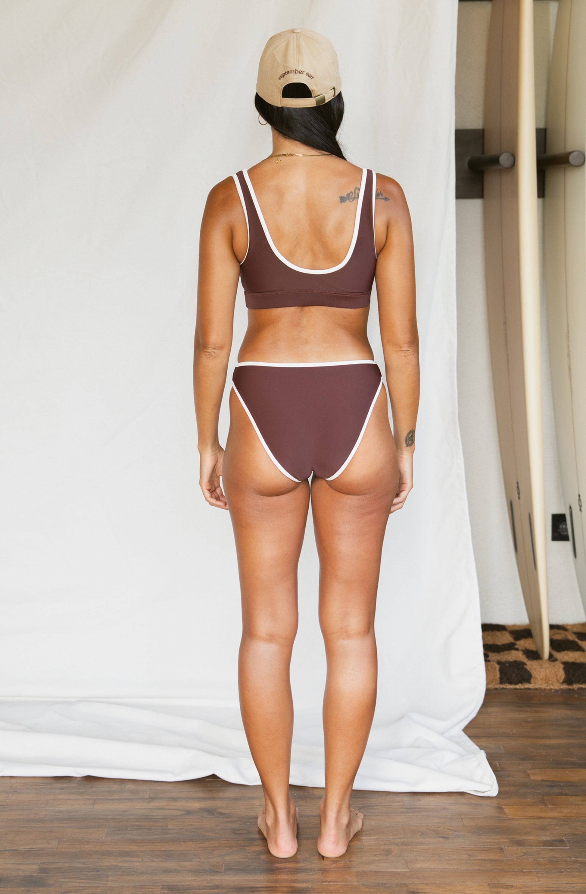 Woman wearing a brown bikini set standing against a white curtain.