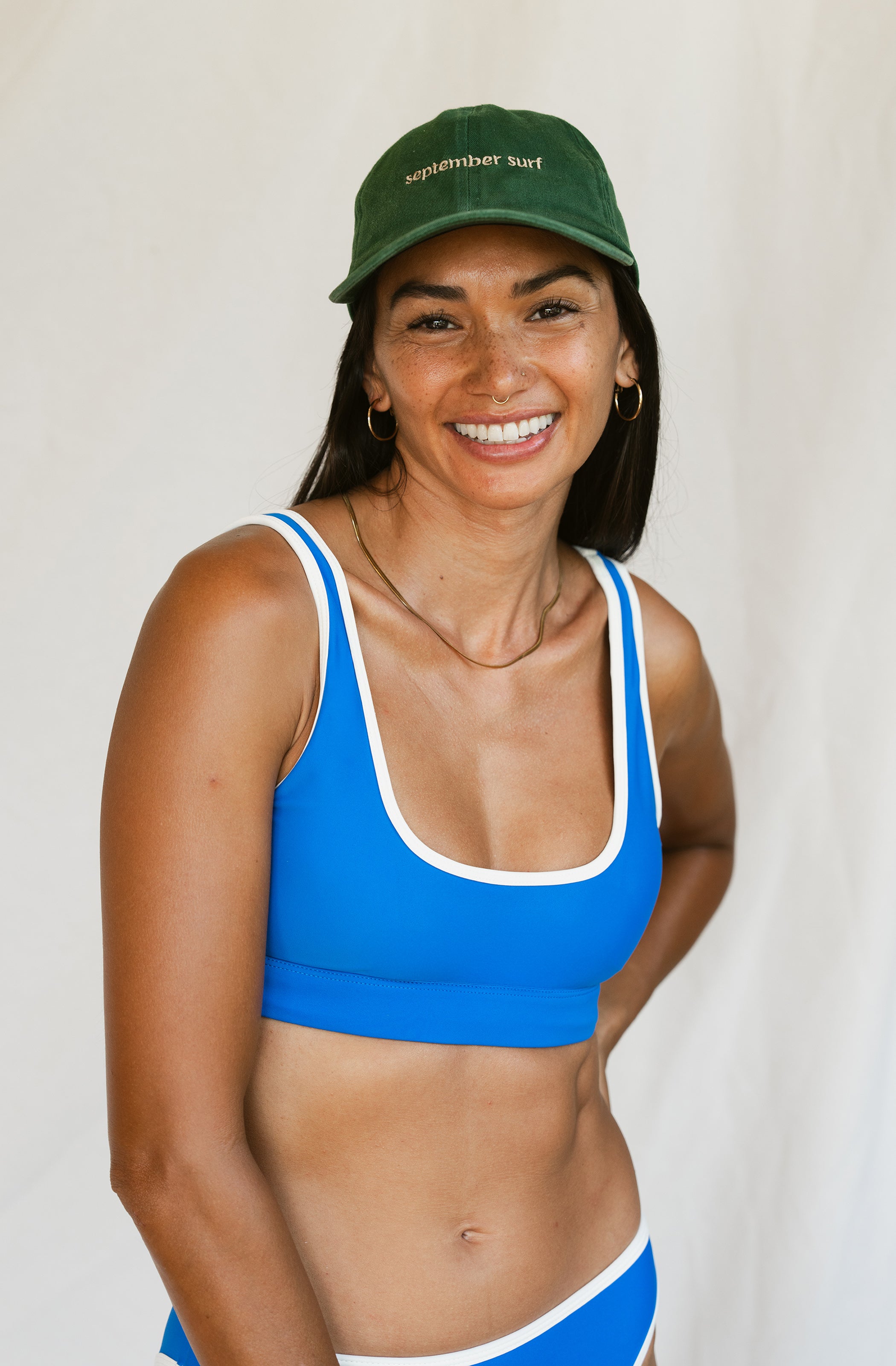 Woman wearing a blue sports bra and green cap with 'September' text on a plain background