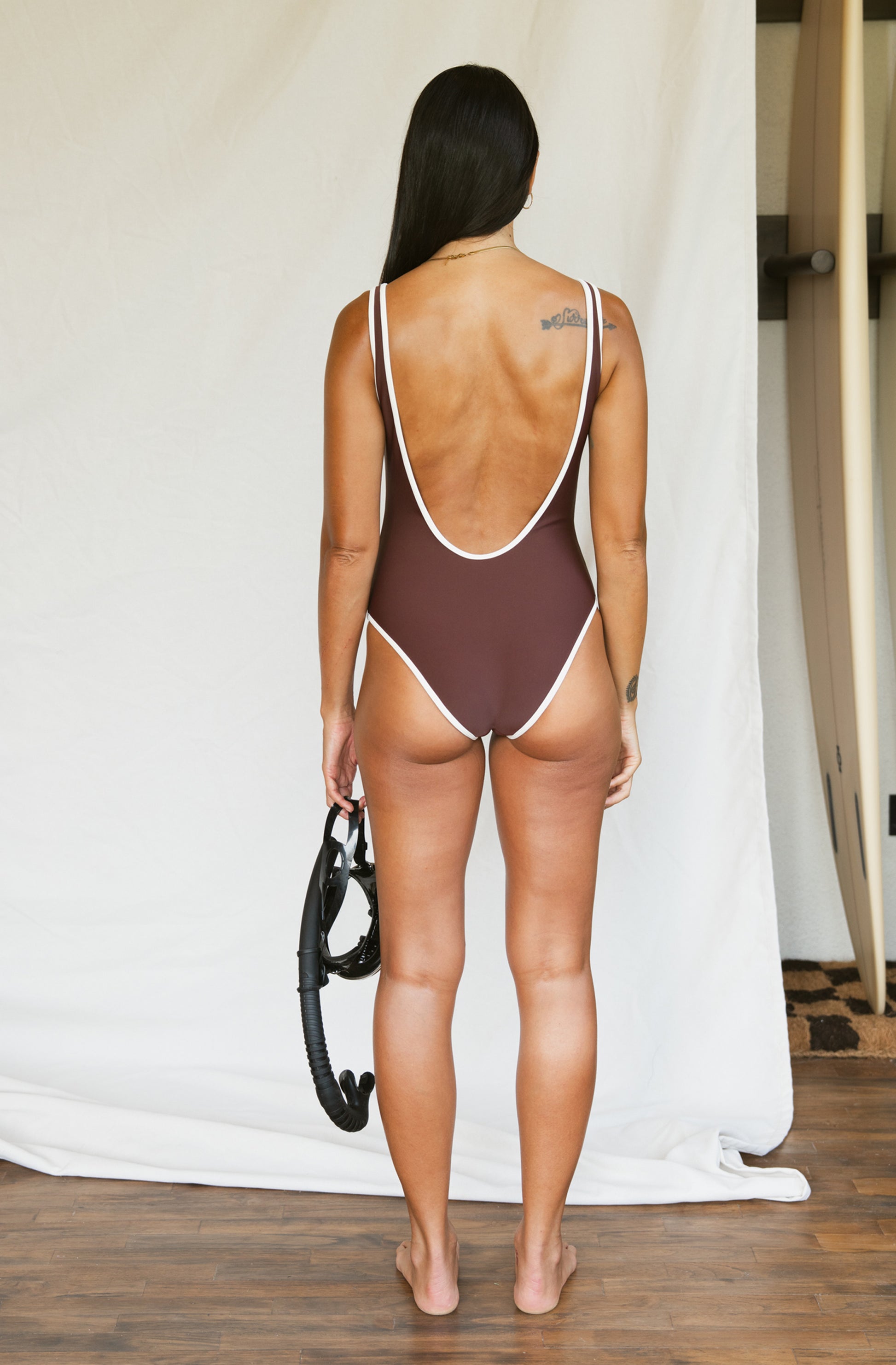 Woman wearing a brown swimsuit with white straps against a plain background
