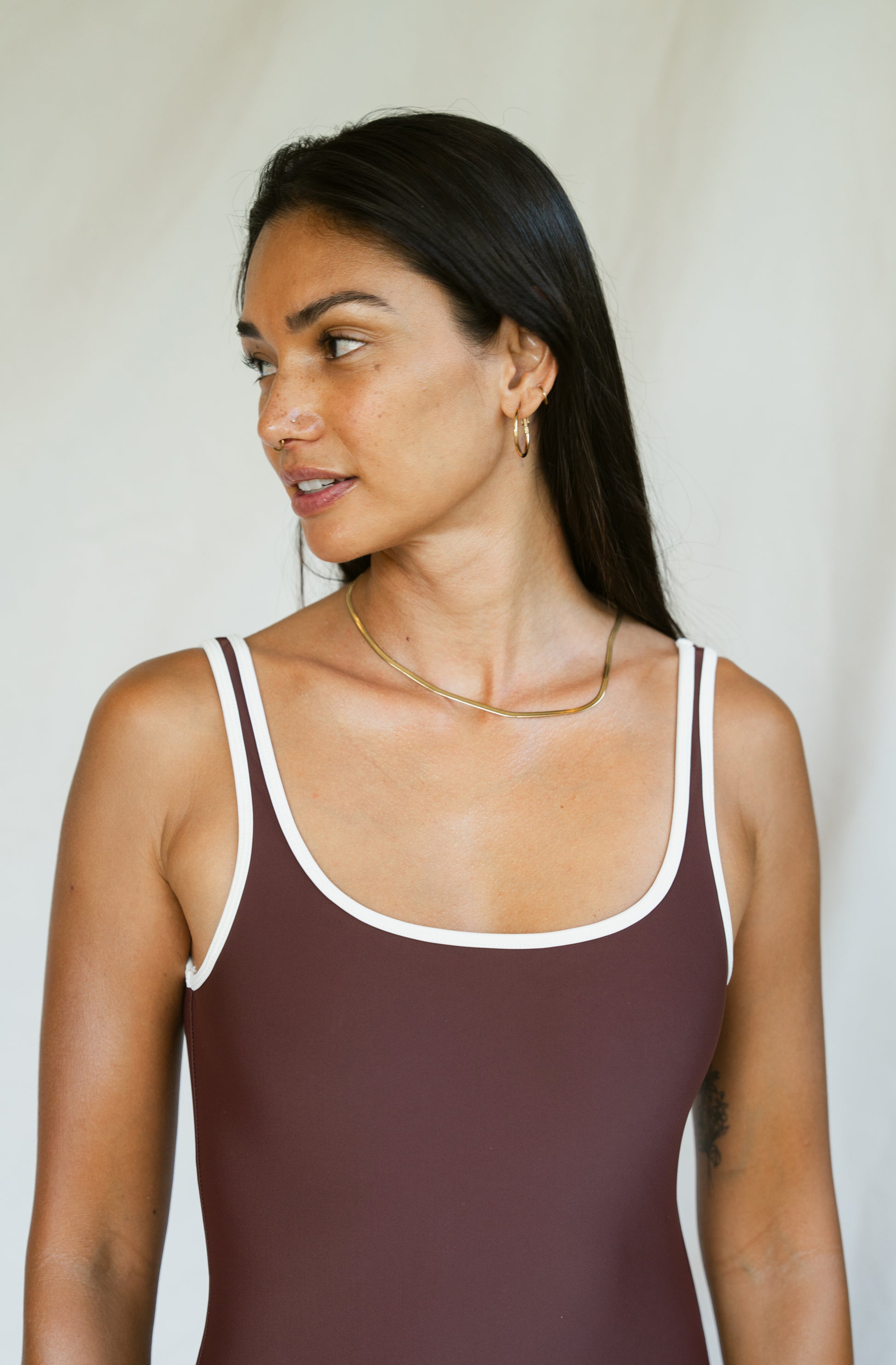 Woman wearing a brown swimsuit with white straps against a plain background