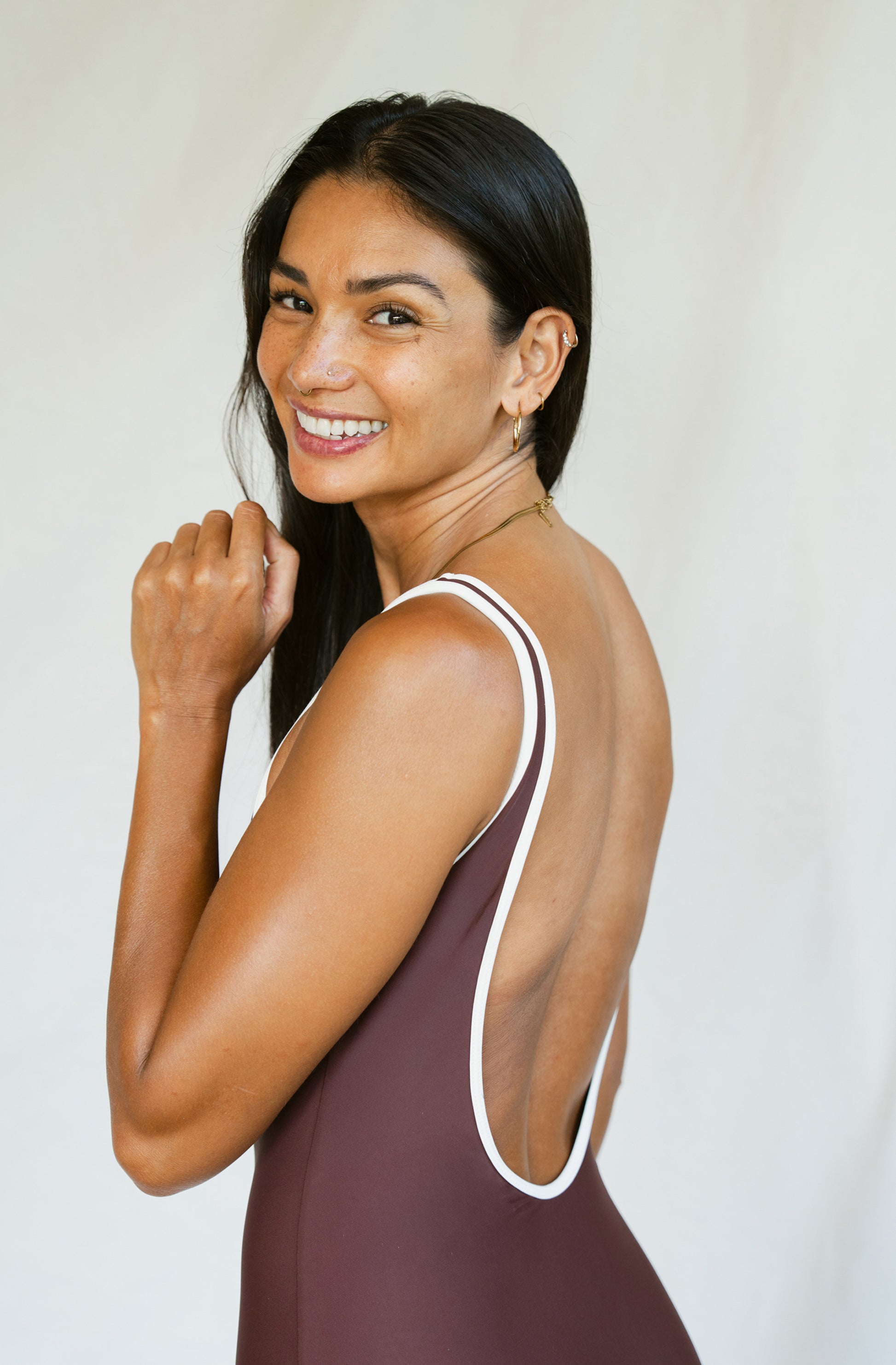 Woman wearing a brown swimsuit with white straps against a plain background