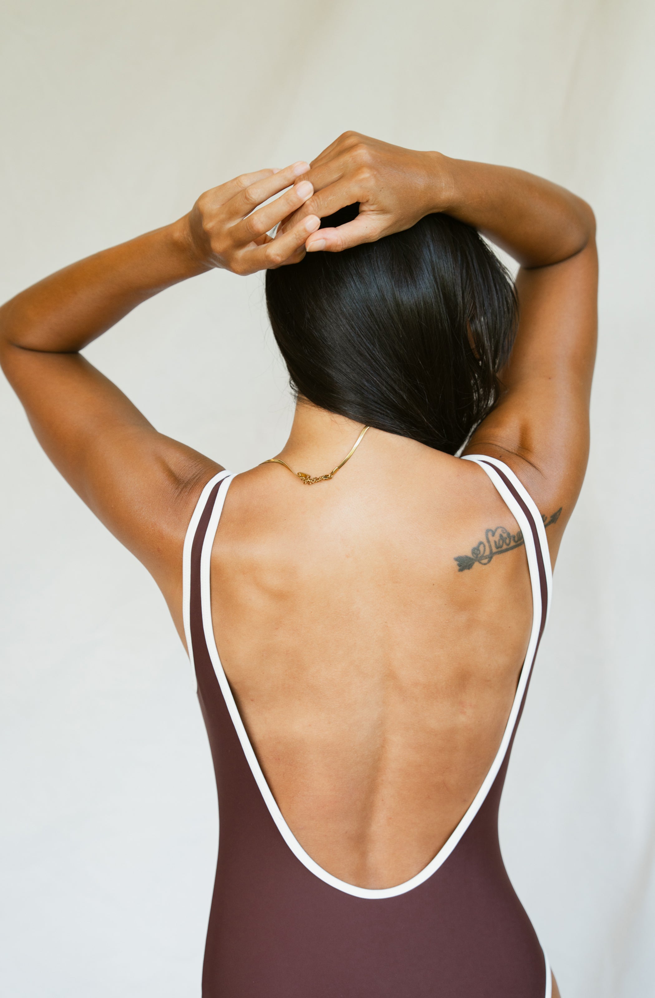 Woman wearing a brown swimsuit with white straps against a plain background
