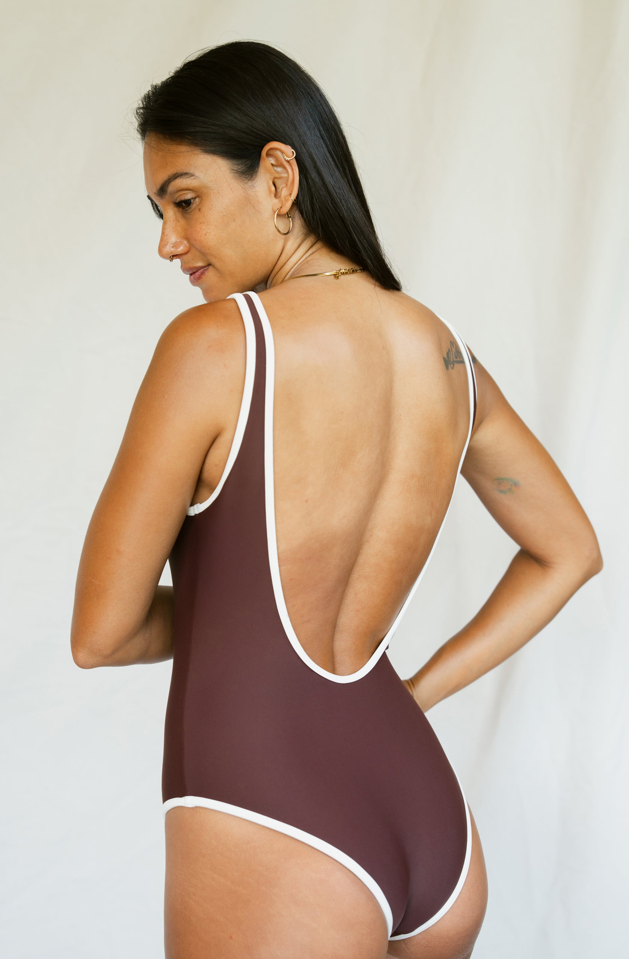 Woman wearing a brown swimsuit with white straps against a plain background