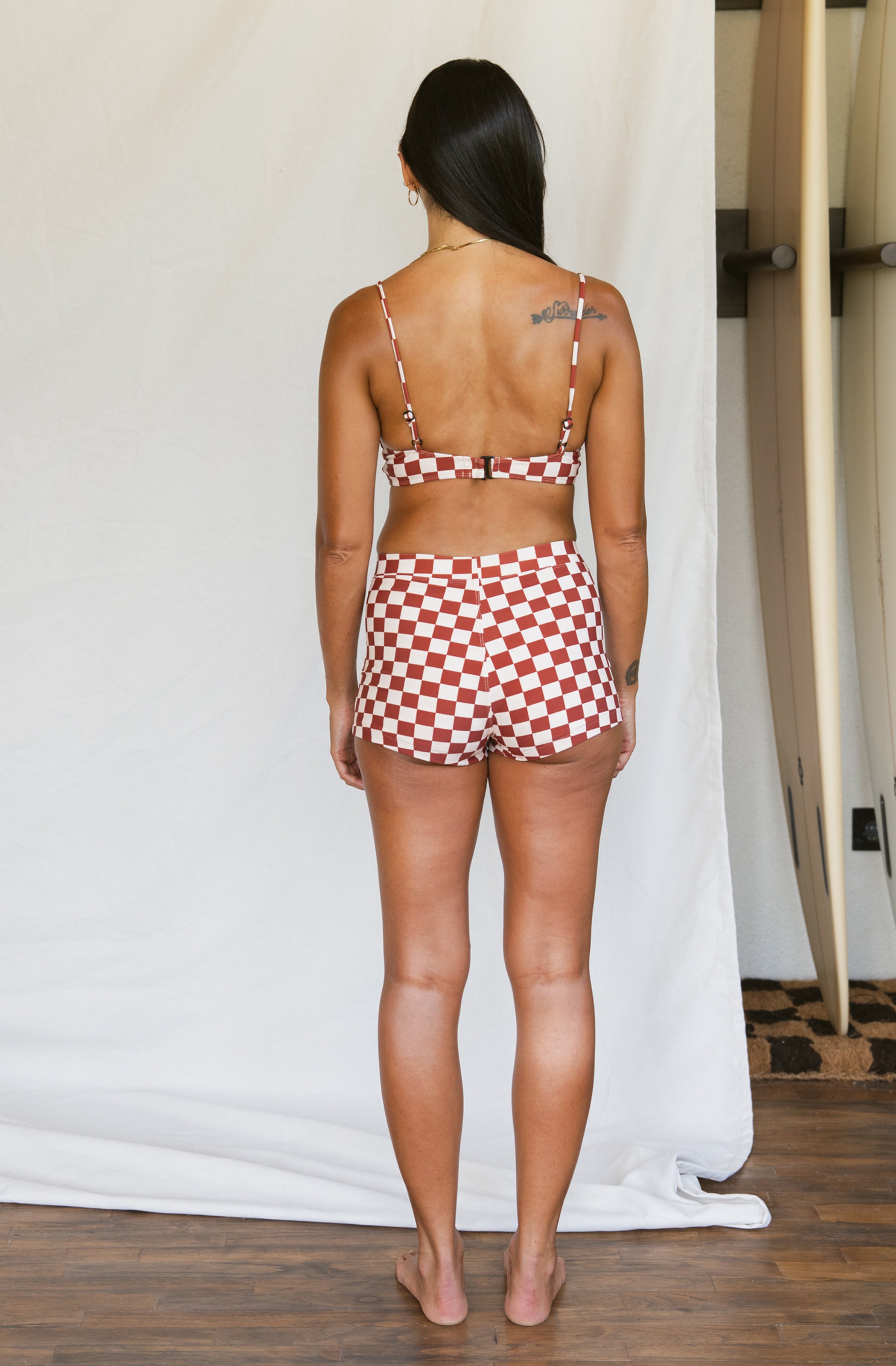 Woman wearing a red and white checkered bikini set in a minimal indoor setting.
