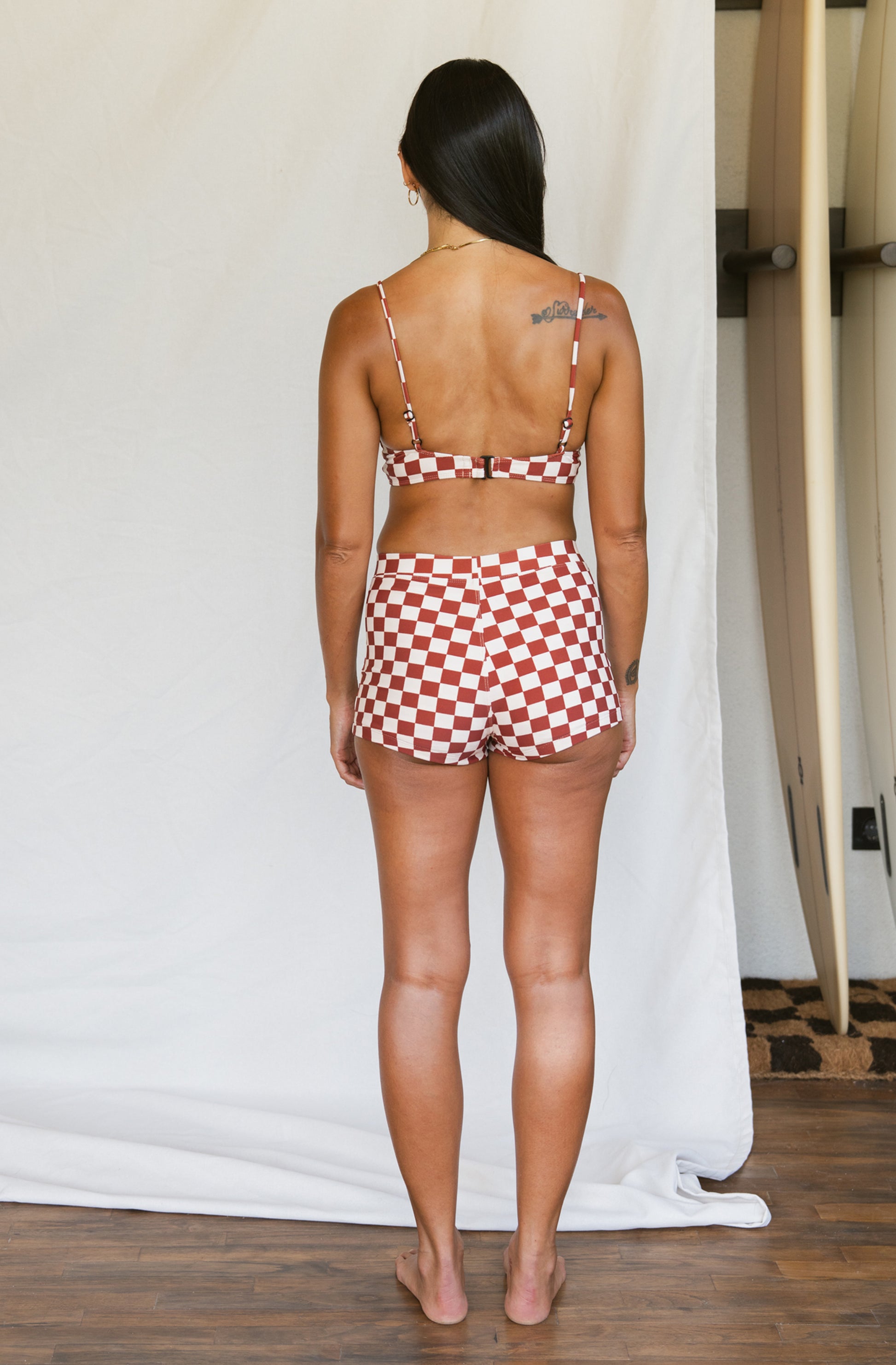 Woman wearing a red and white checkered bikini set in a minimal indoor setting.