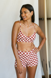 Woman wearing a red and white checkered bikini set standing against a neutral background.