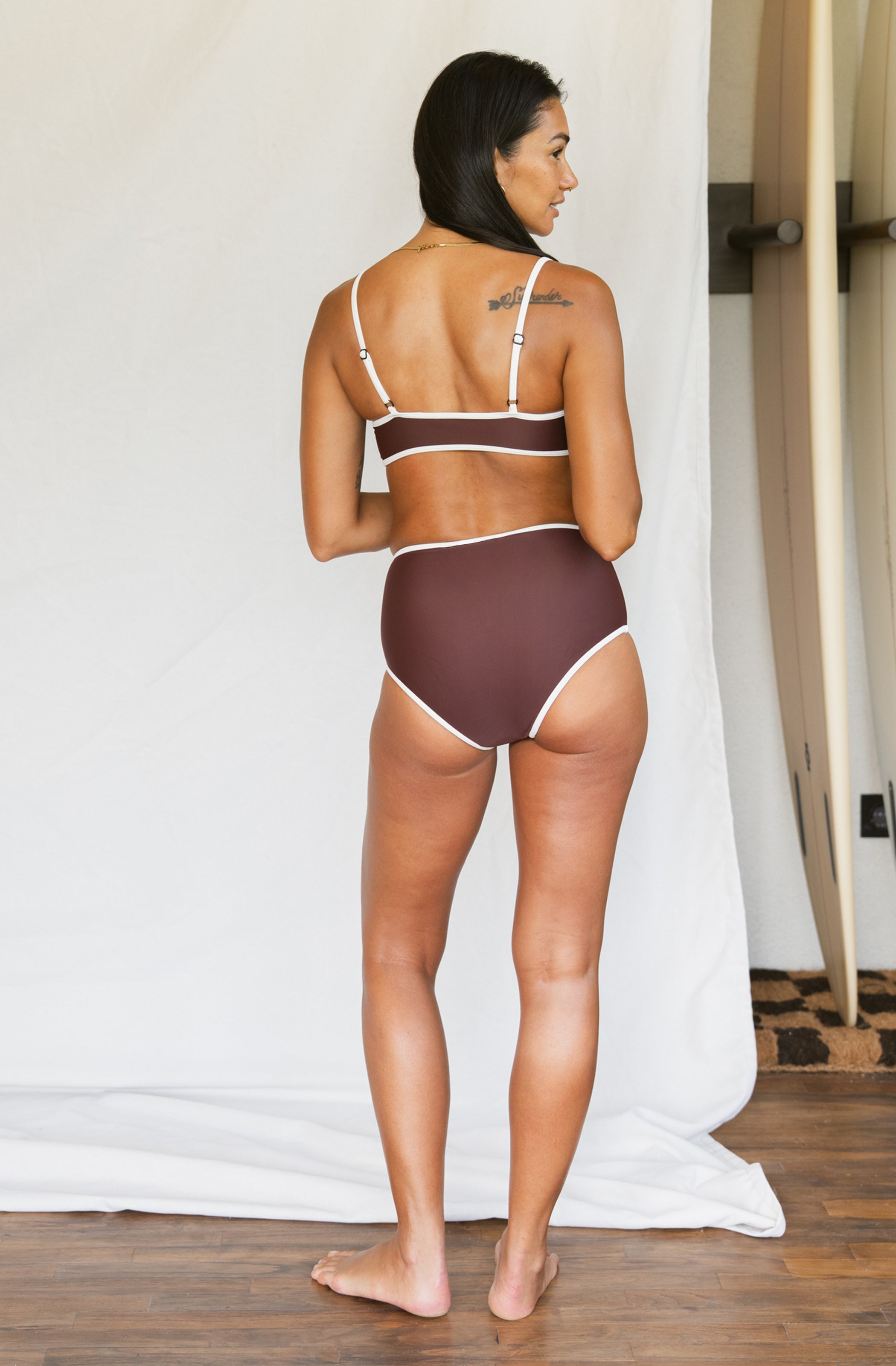 Woman wearing a brown bikini with white trim in a minimal indoor setting