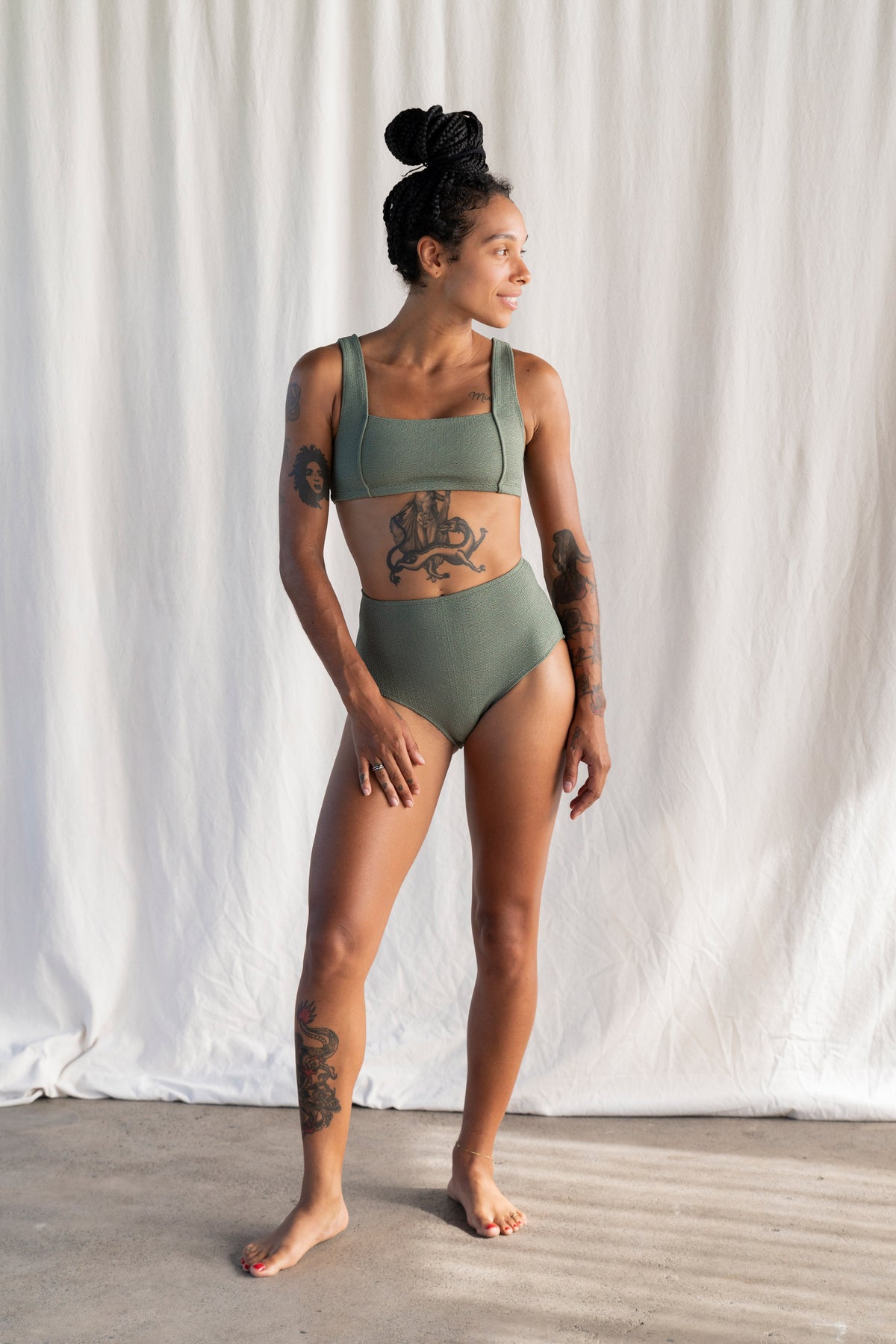 Woman wearing a green bikini standing against a white curtain