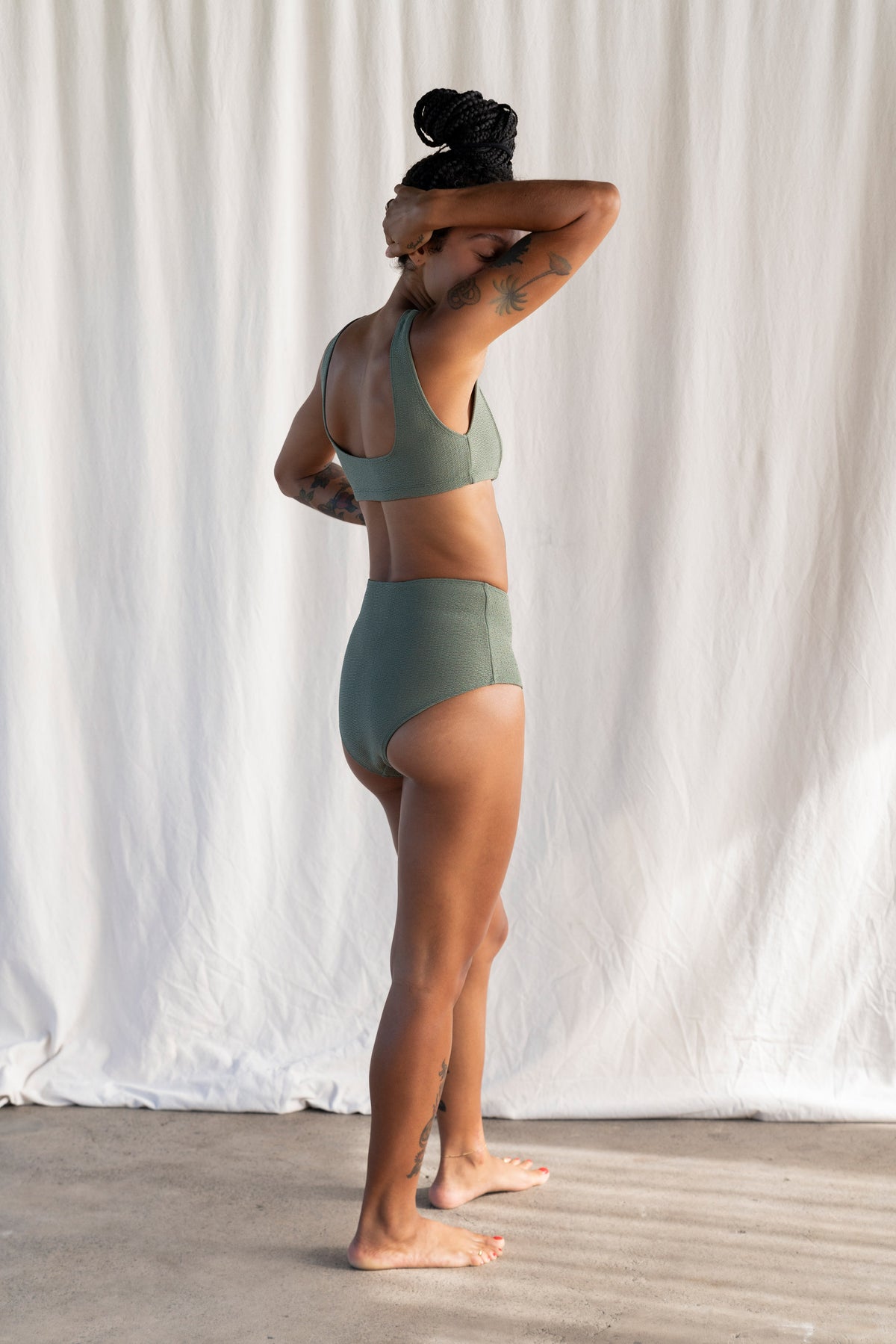 Person wearing a green bikini standing against a white curtain.