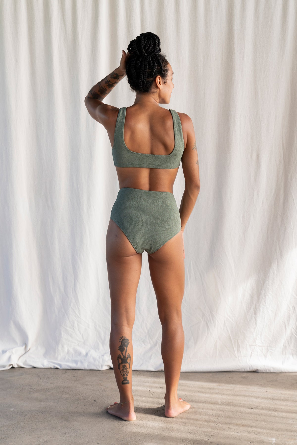Woman wearing a green bikini standing against a white curtain.
