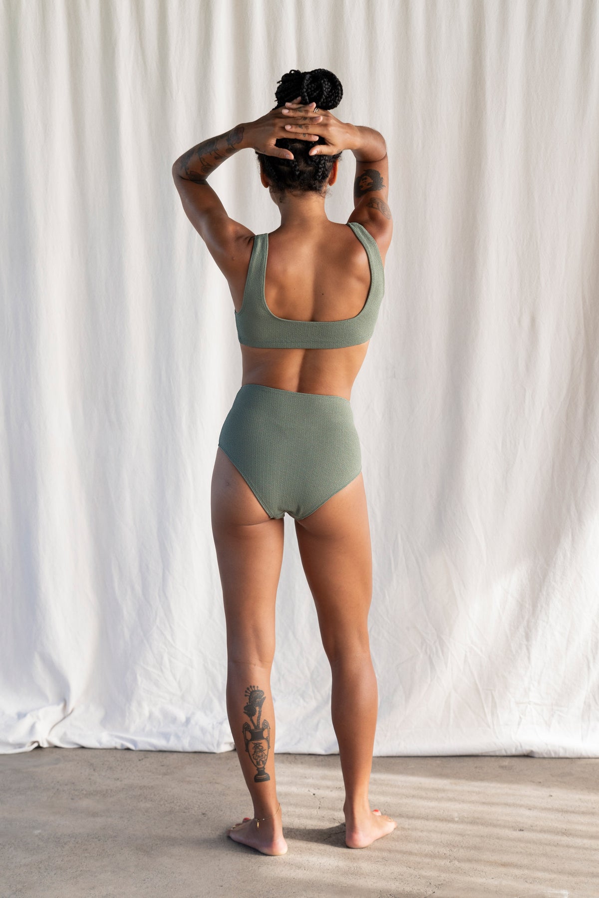 Person wearing a green sports bra and high-waisted shorts against a white curtain background