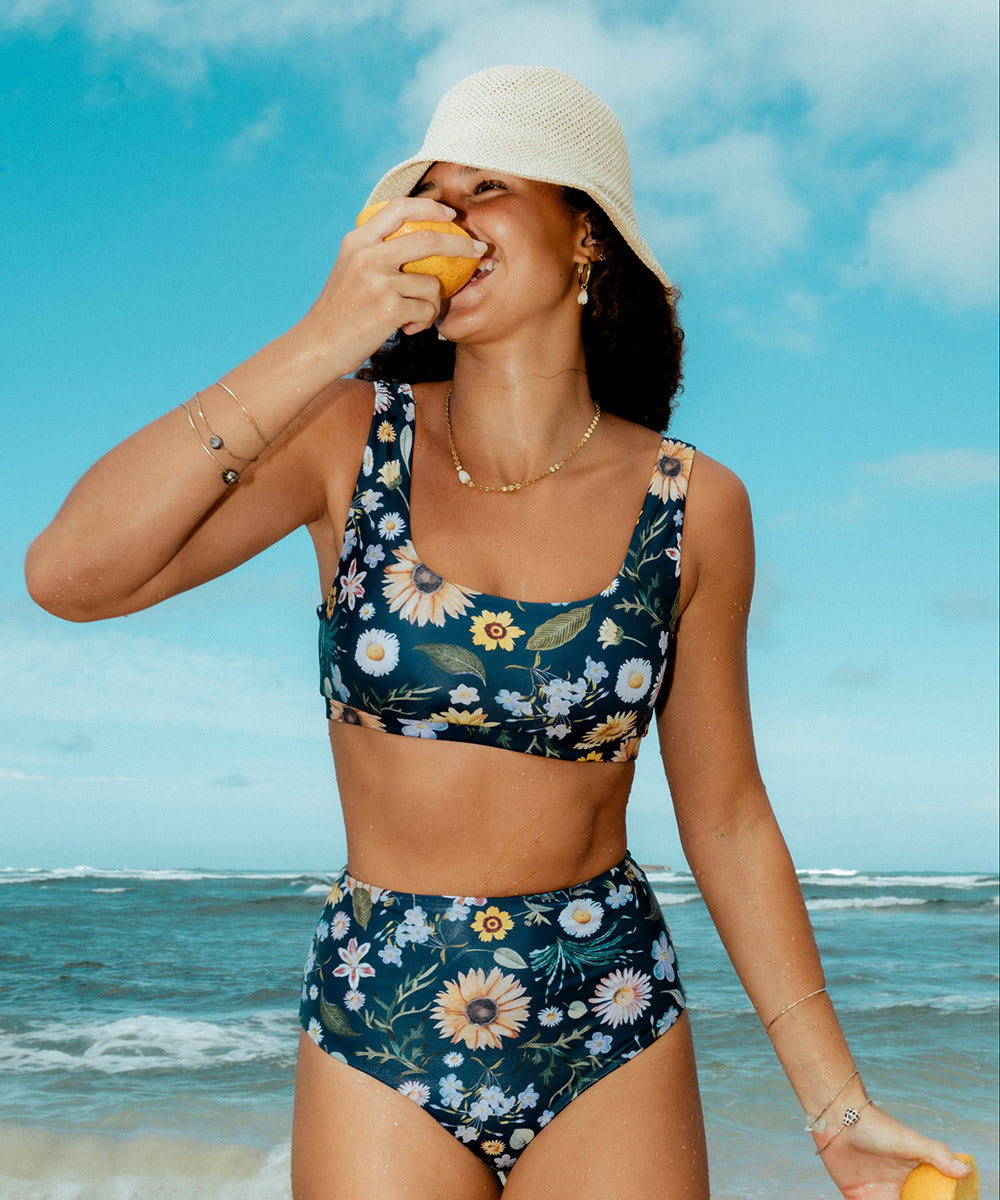 Woman in a floral bikini at the beach eating an orange.