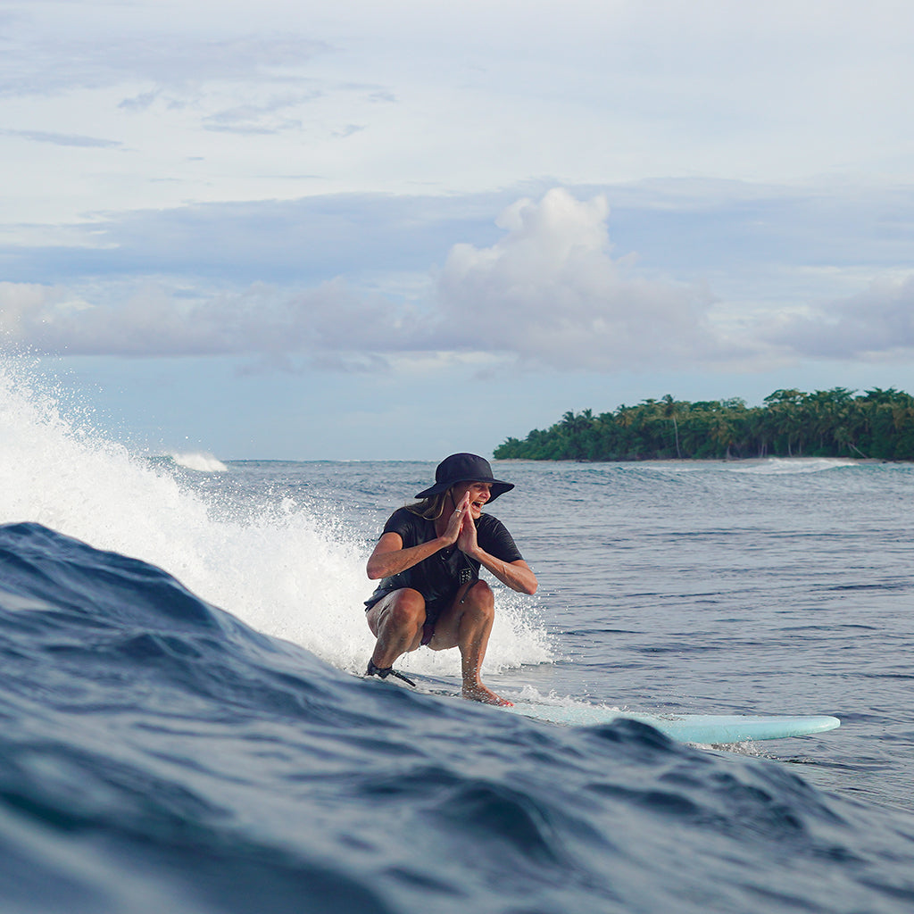 woman crouching down on a surfboard with a huge smile on her face