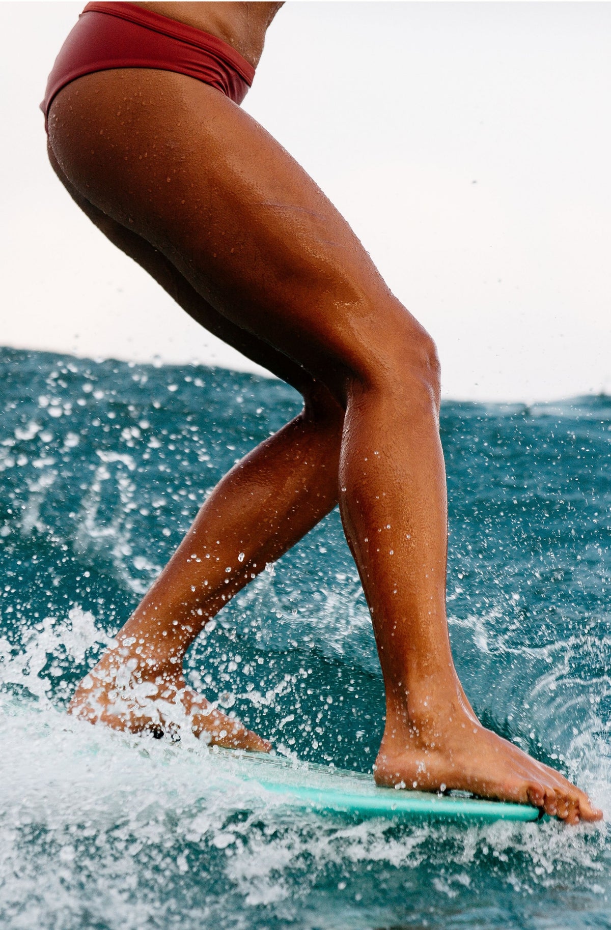 Close shot of a woman longboarding on a wave wearing a surf bikini bottom in burnt sienna. 