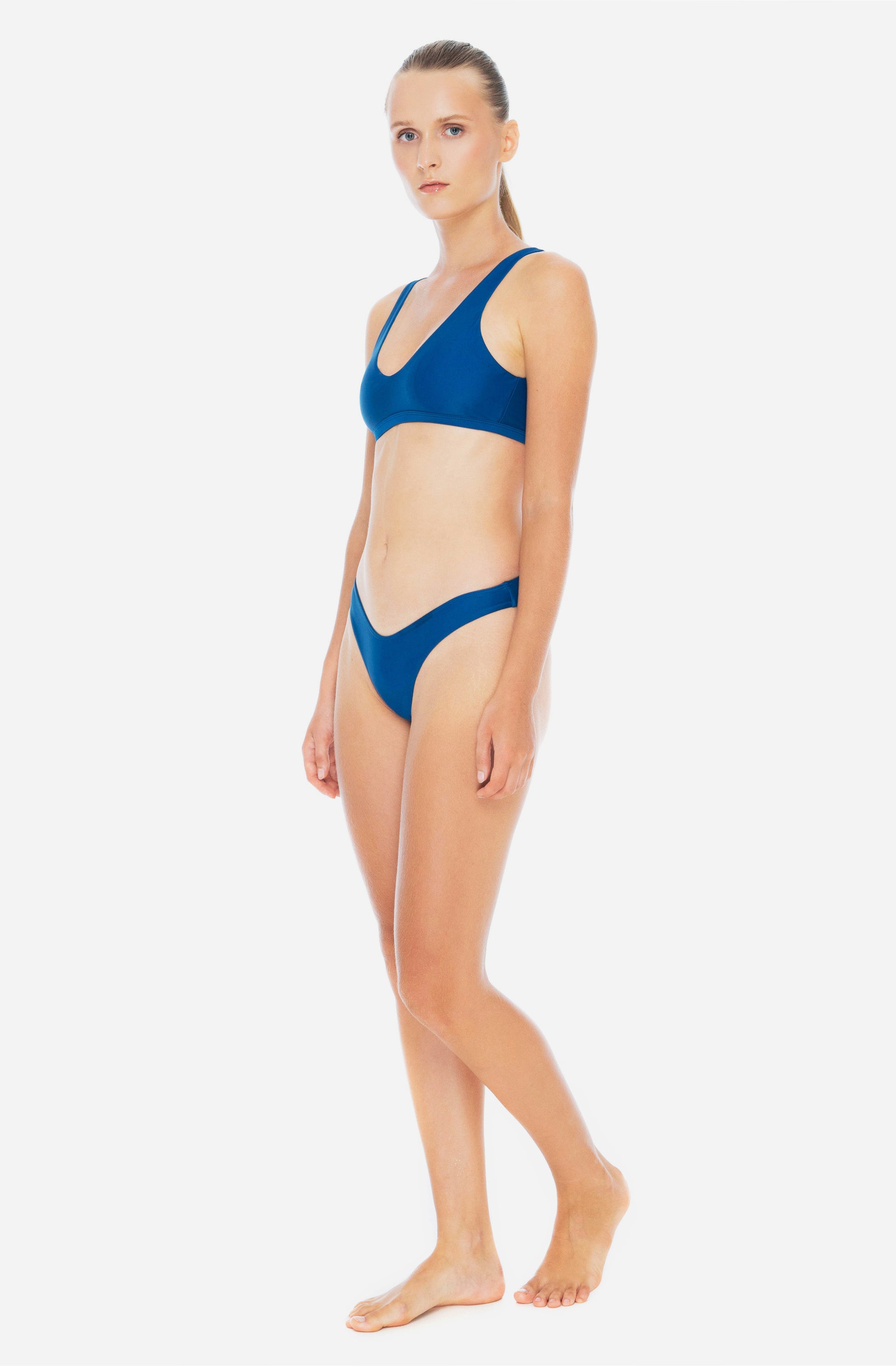 Side view of  woman wearing triangle top surf bikini top and bottom in lake blue