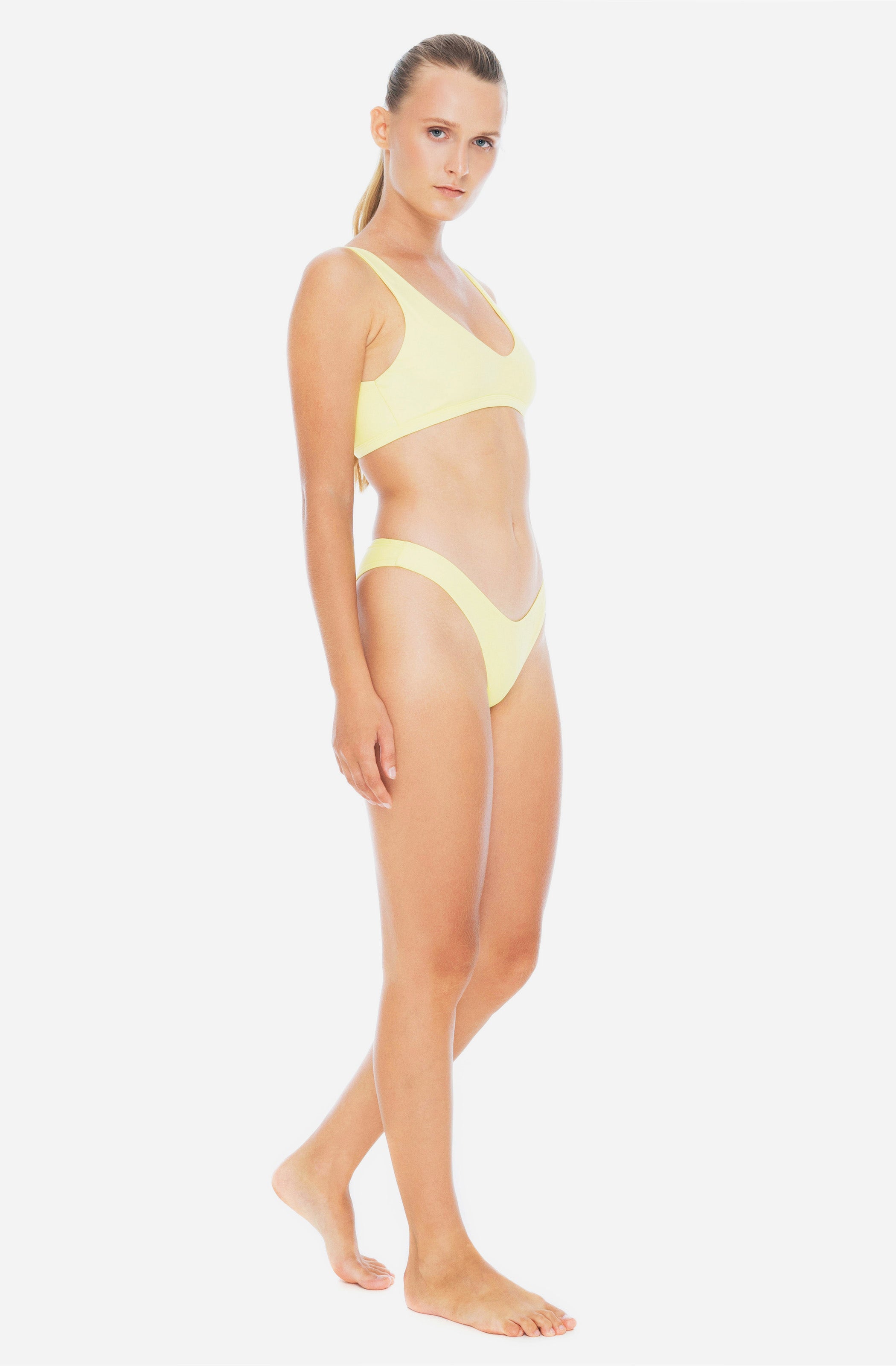 Side profile view of a woman modelling a surf bikini top and a surf bikini bottom in sunflower yellow.