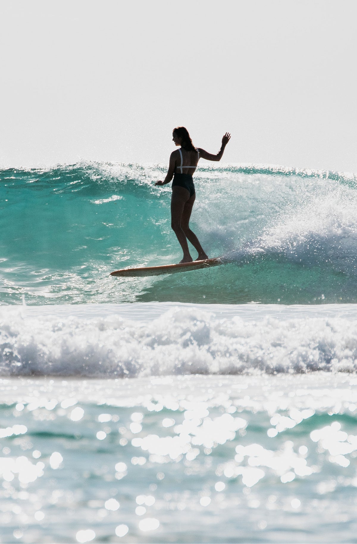 Shot of a woman on a longboard wearing a one piece surf swimsuit in army green.