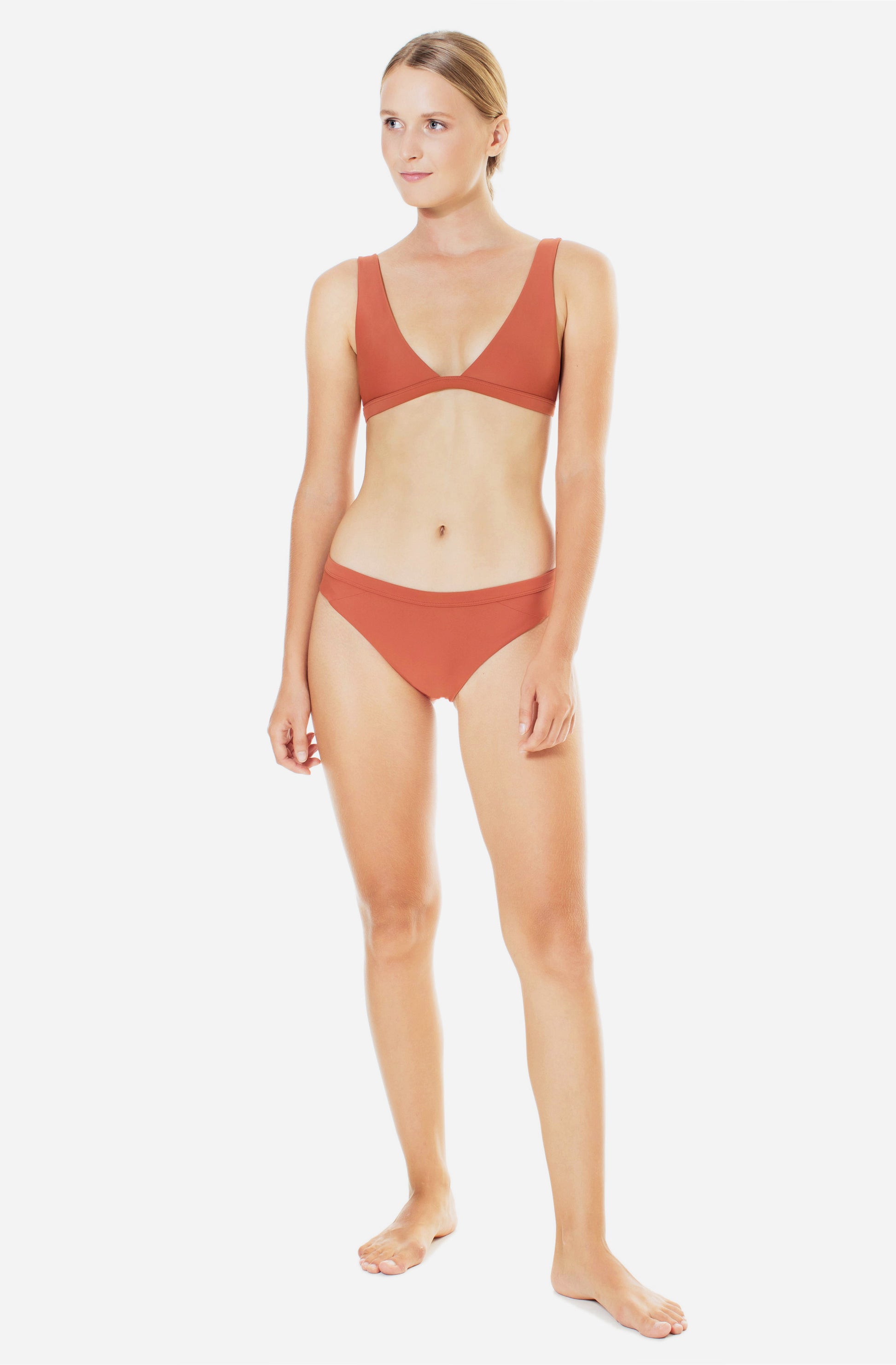Front view of a woman modelling a triangle bikini top and a surf bikini bottom in burnt Sienna.