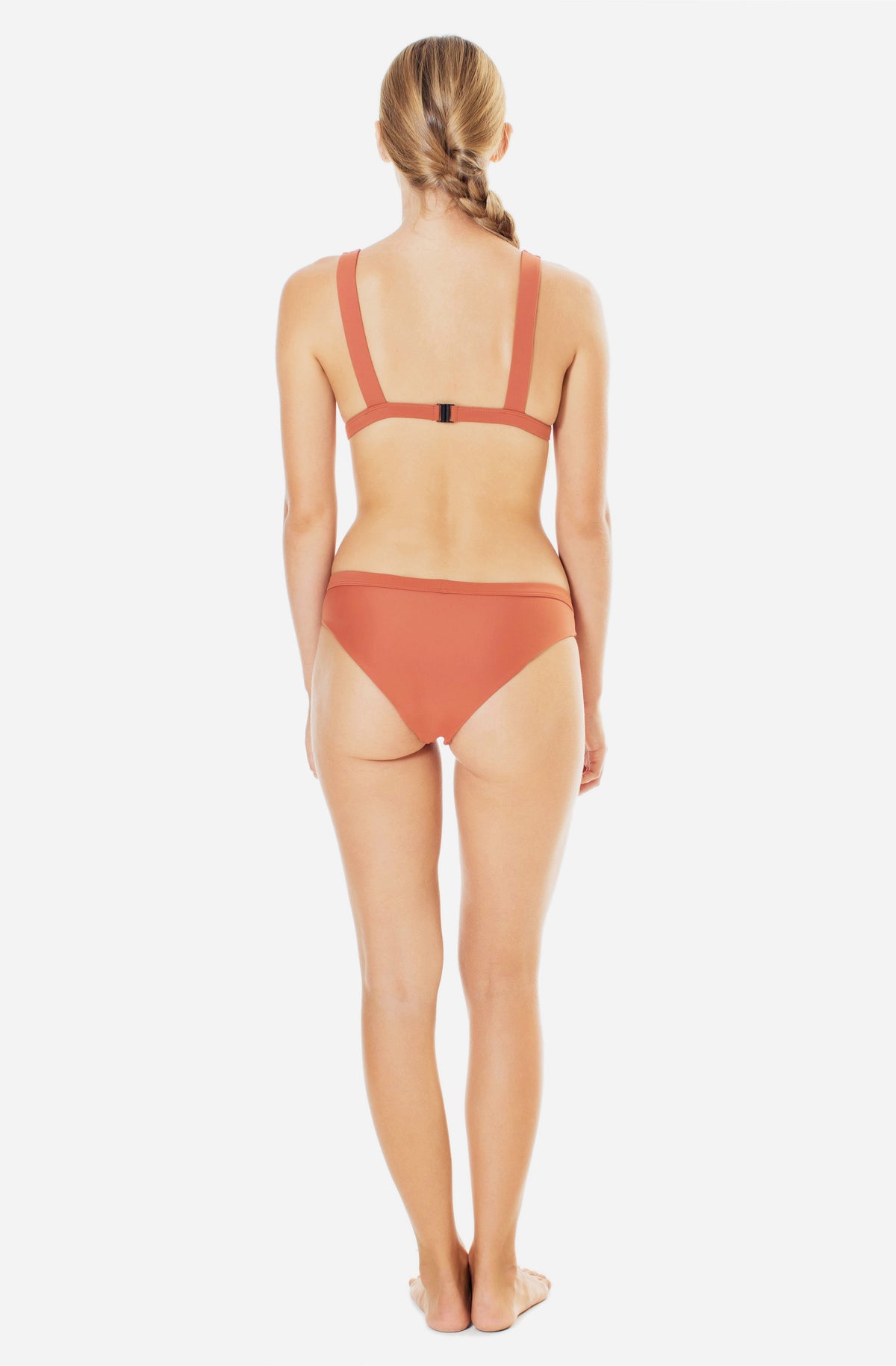 Back view of a woman modelling a triangle bikini top and a surf bikini bottom in burnt Sienna.
