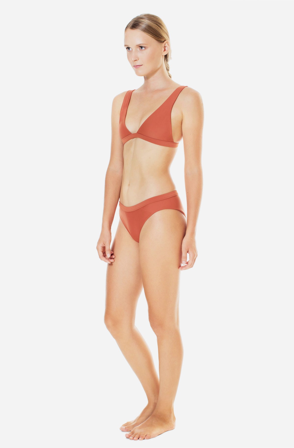 Side profile view of a woman modelling a triangle bikini top and a surf bikini bottom in burnt Sienna. 