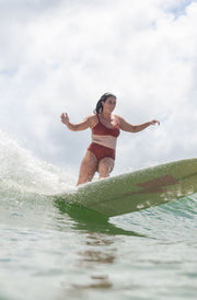 Woman doing a carving turn in the lori bikini top and Alice bikini bottom in Burnt Sienna