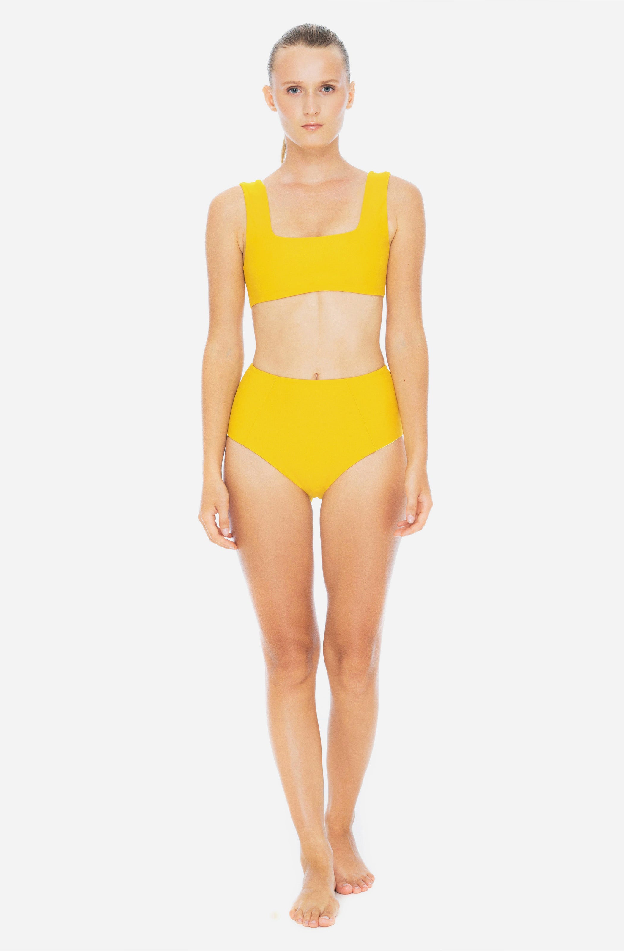 Front view of a woman wearing a surf bikini top and a high-waisted bikini bottom in saffron yellow.