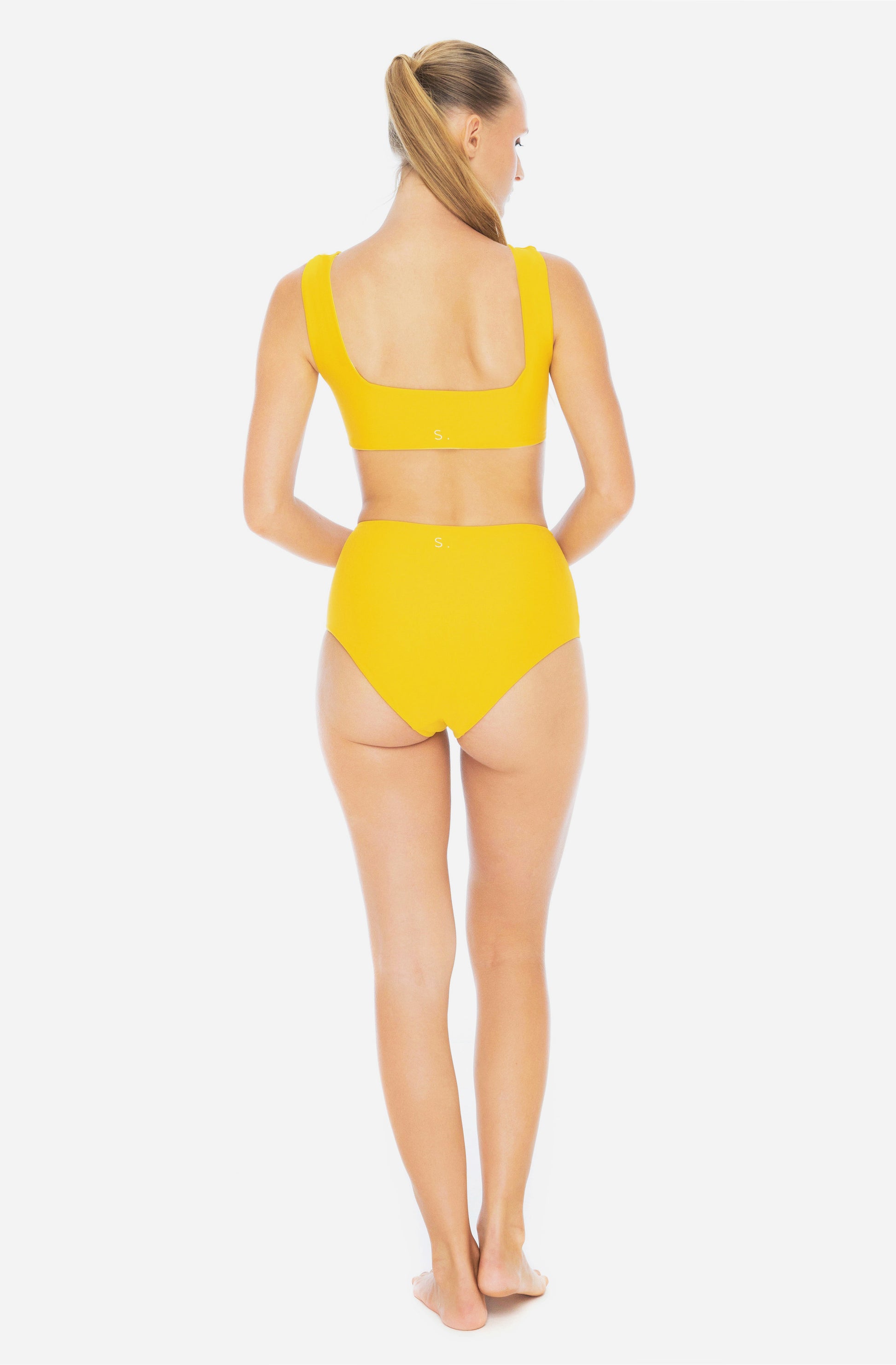 Back view of a woman modelling a surf bikini top and a high-waisted bikini bottom in saffron yellow.
